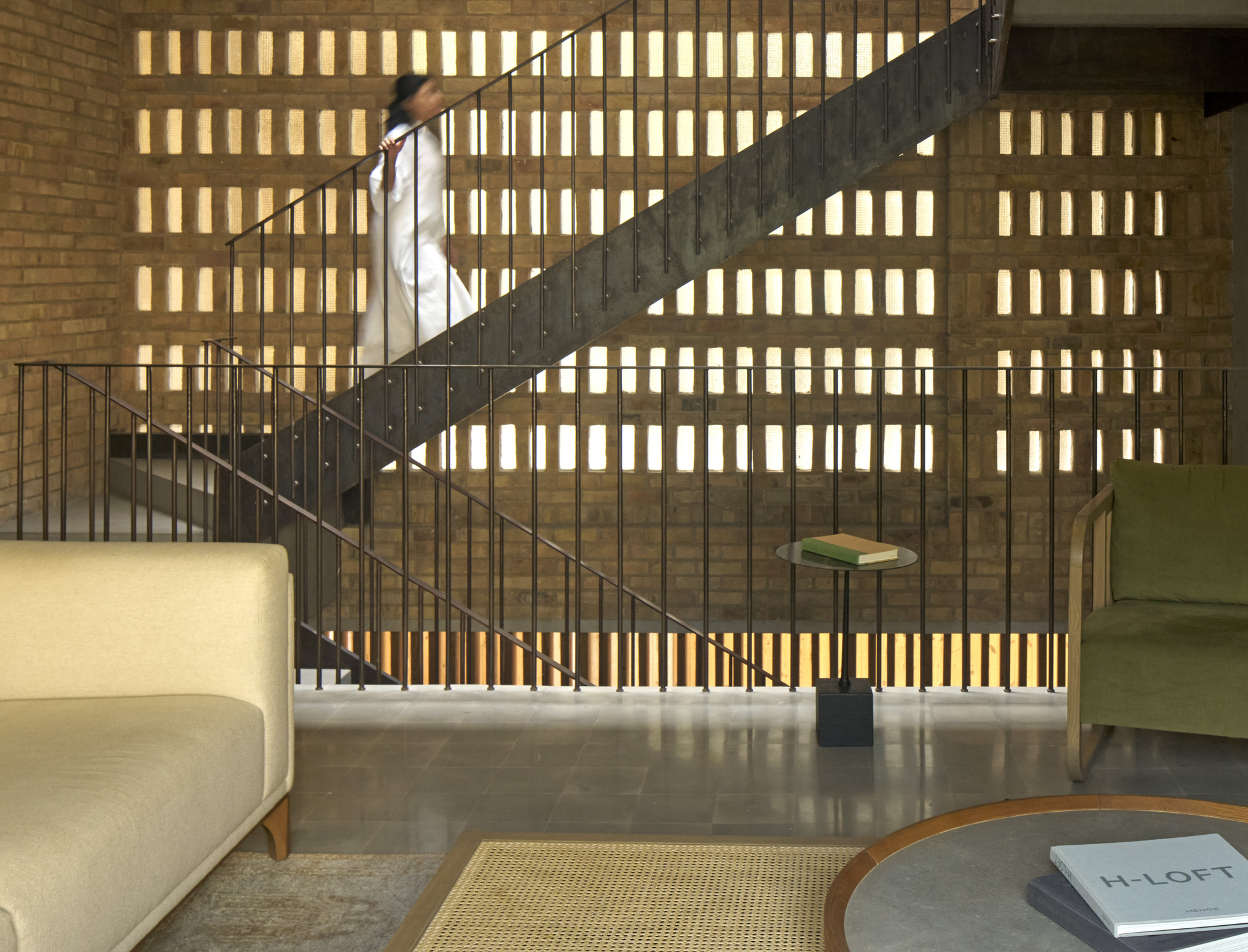 Curved steel staircase rising against brick wall with backlit vertical openings