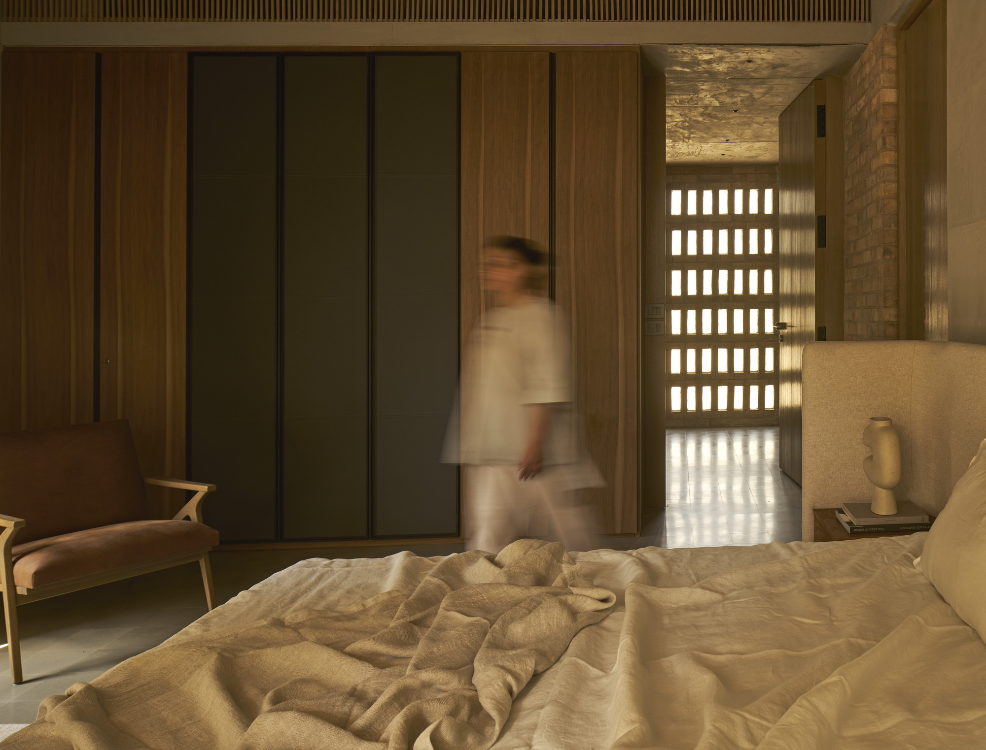 Bedroom with gridded brick screen wall and blurred figure walking through doorway at dusk