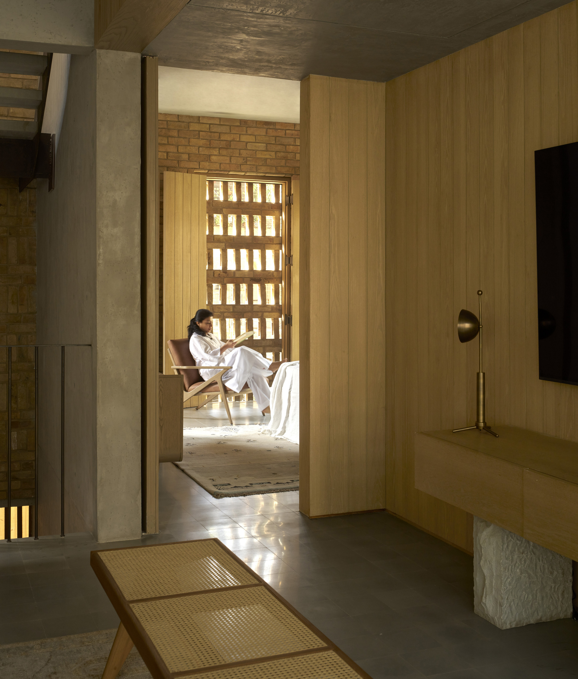 View through timber-lined hallway toward seating alcove with gridded brick light screen