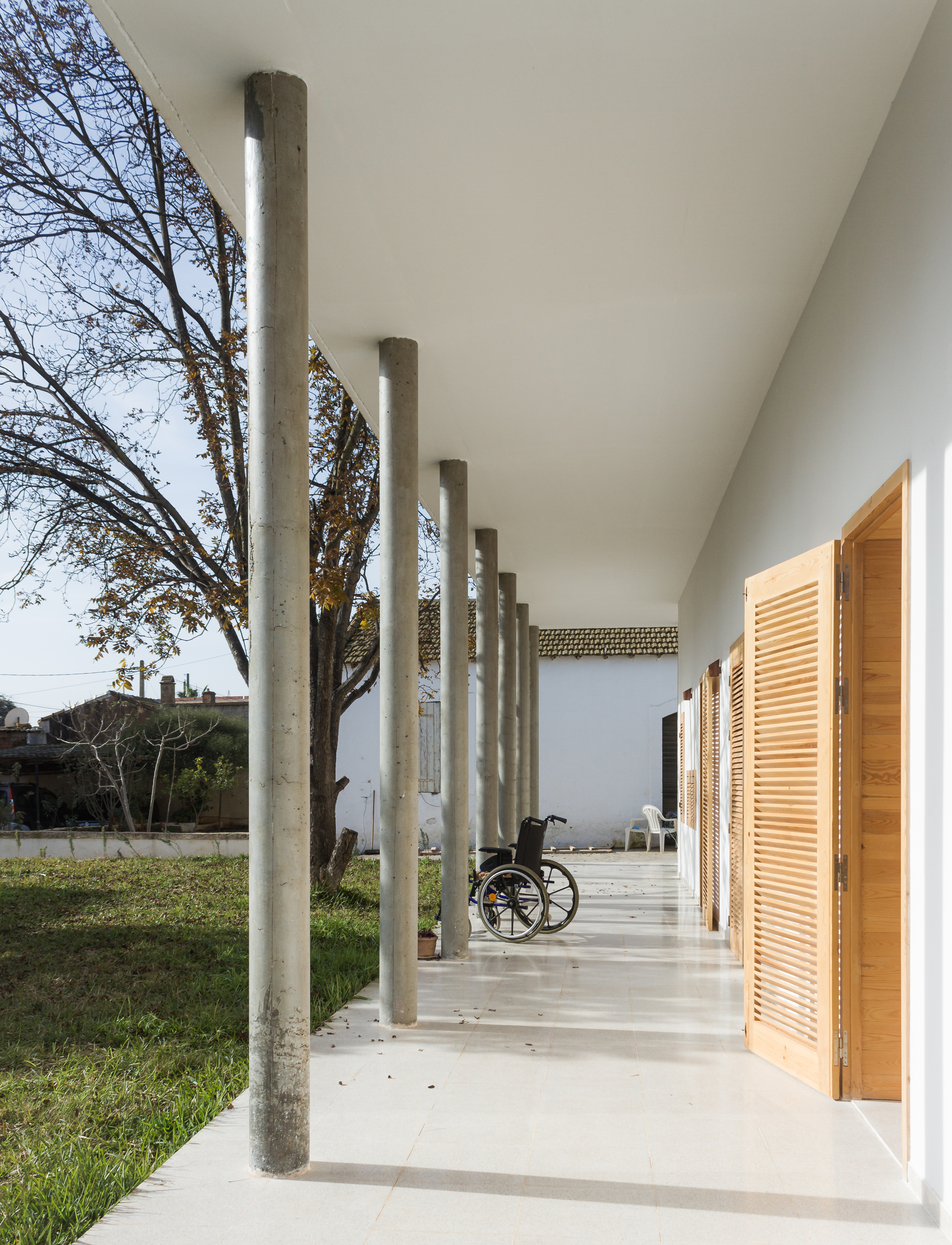Long colonnade with cylindrical concrete supports and wheelchair visible at far end in afternoon light
