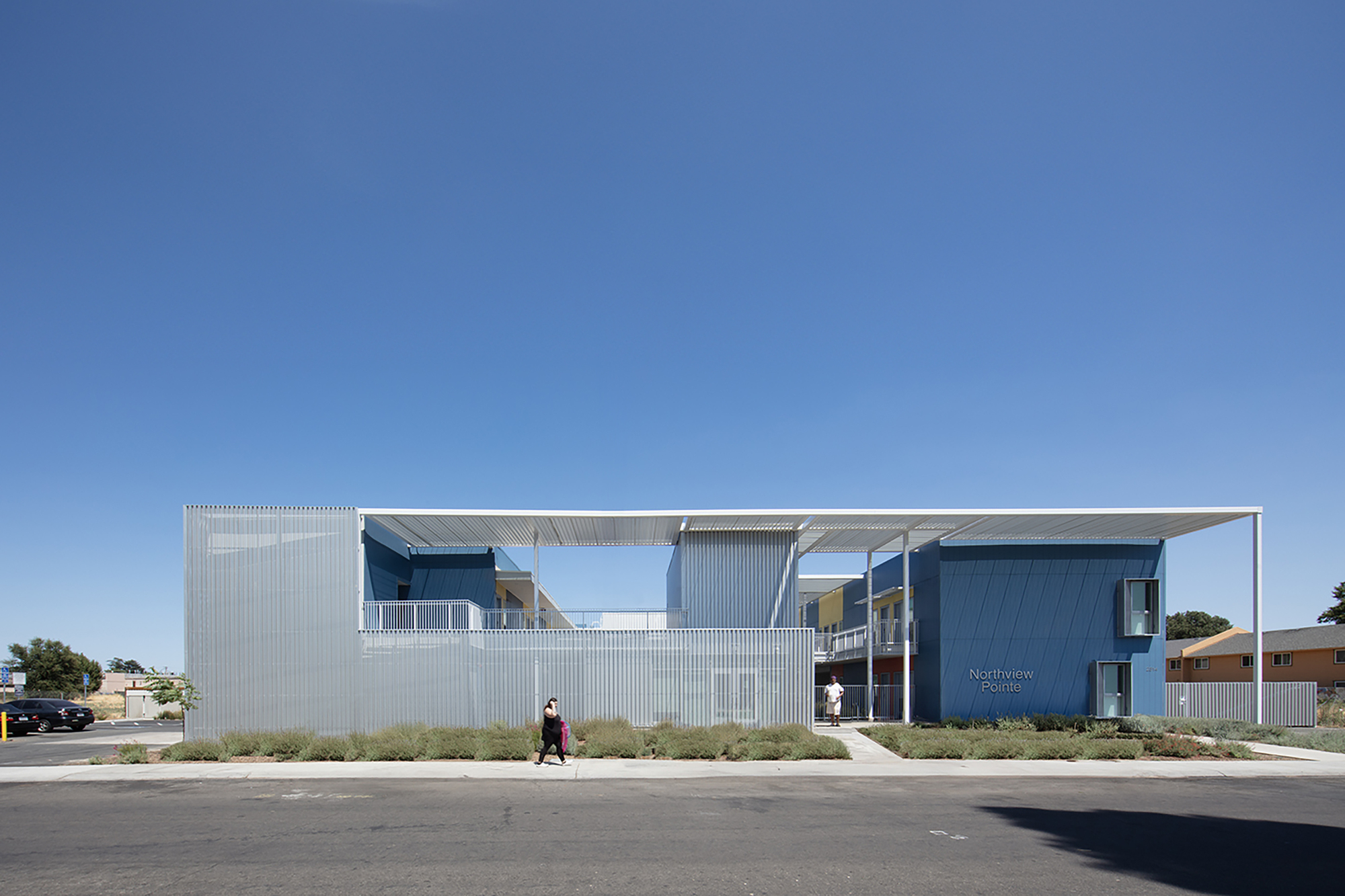 Street view of the corrugated metal facade with upper level canopy and a pedestrian walking past