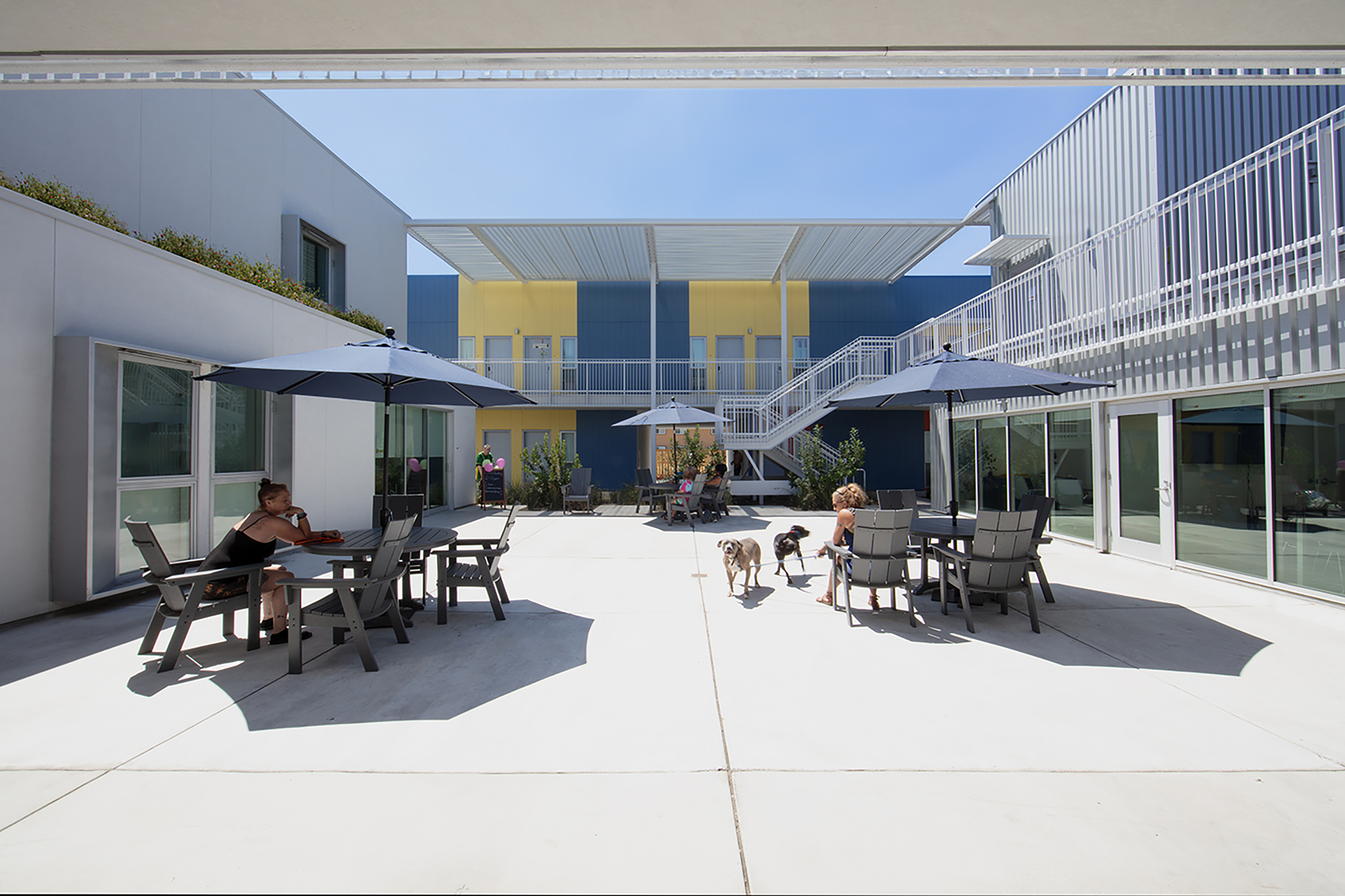 Central courtyard with concrete paving and outdoor furniture between two-story wings with corrugated metal canopies