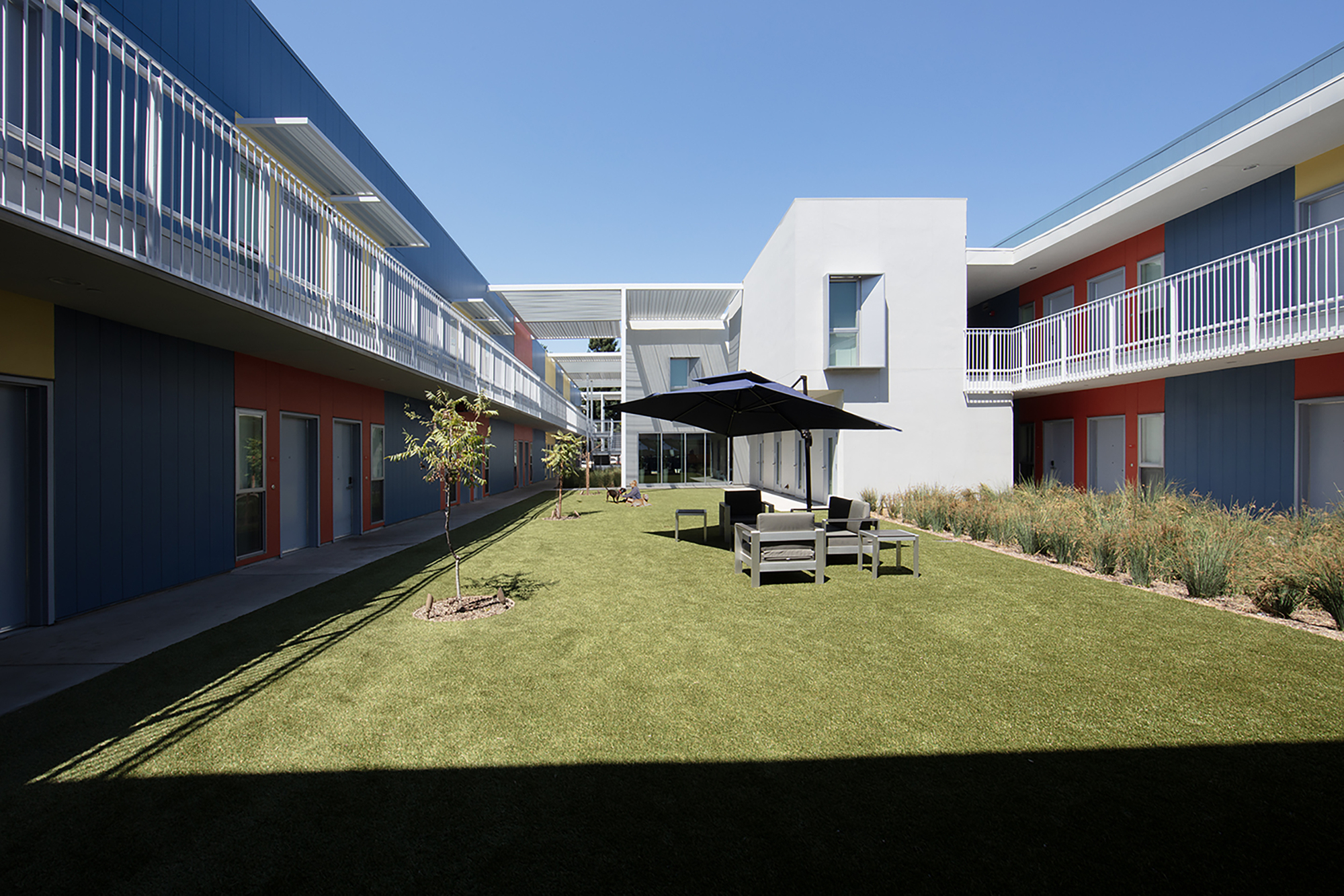 Courtyard lawn framed by residential units with blue and orange panel facades and upper-level walkways