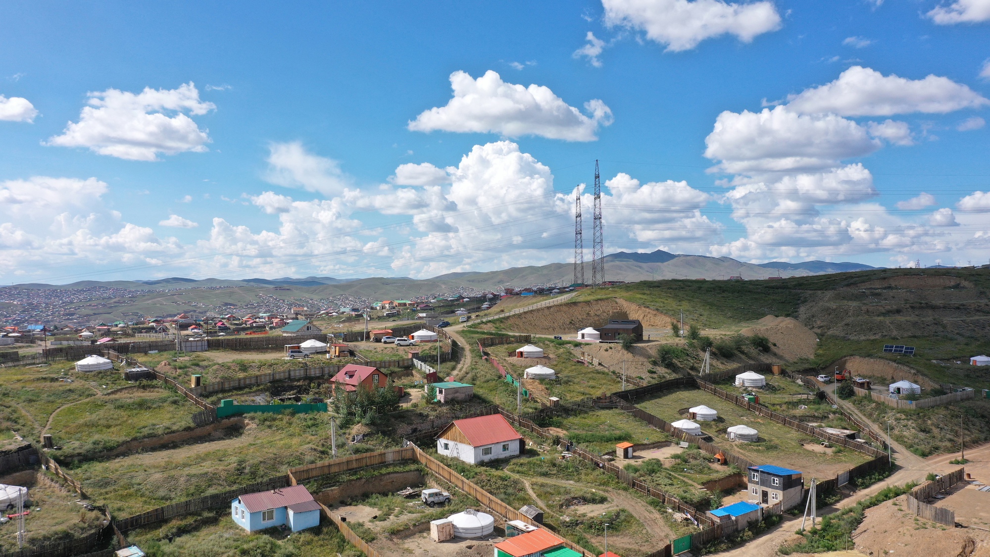 Wide panorama showing two low structures among scattered settlements on rolling grassland under afternoon sky