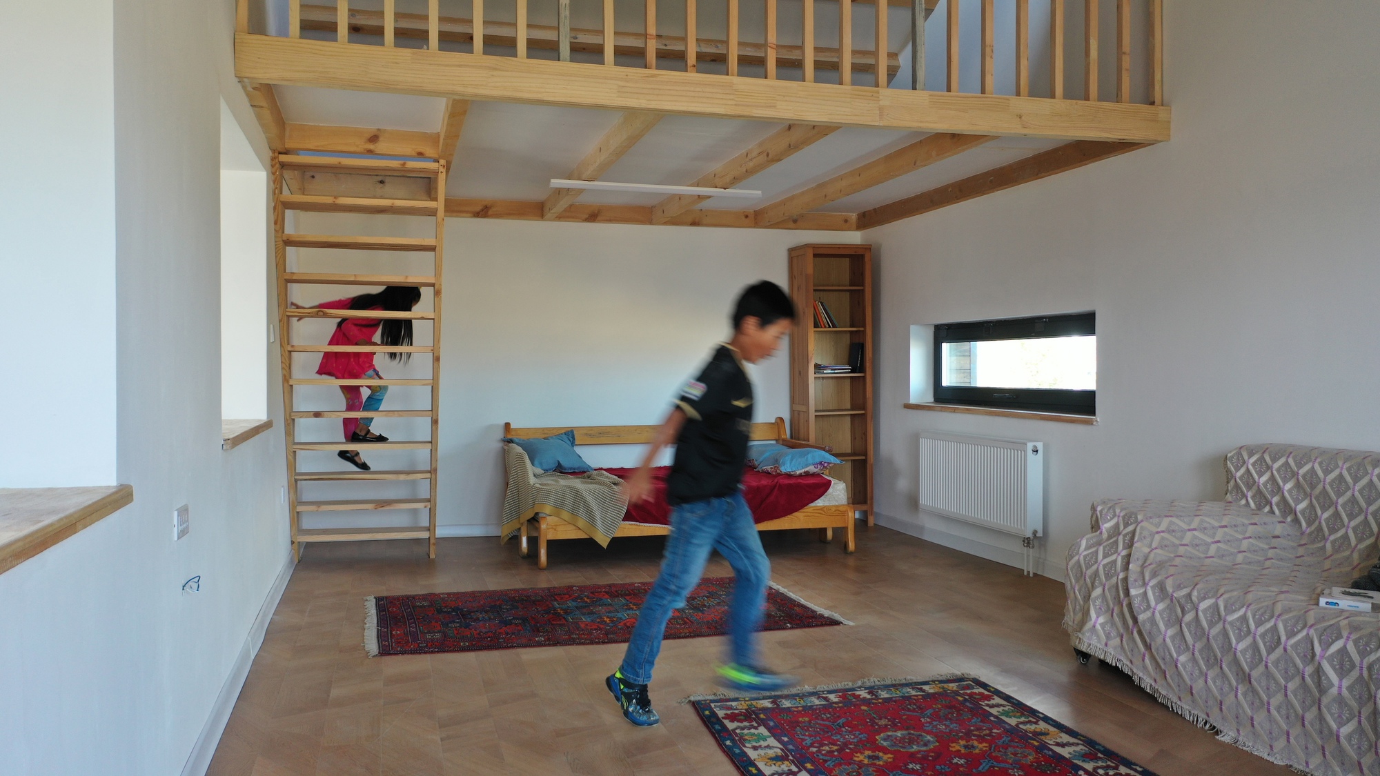 Bedroom with exposed timber joists and ladder access to a loft as a child walks past