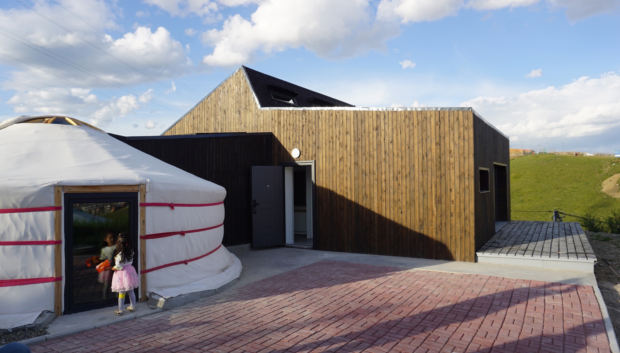 Entry courtyard with brick paving connecting the yurt and the vertical timber-clad volume