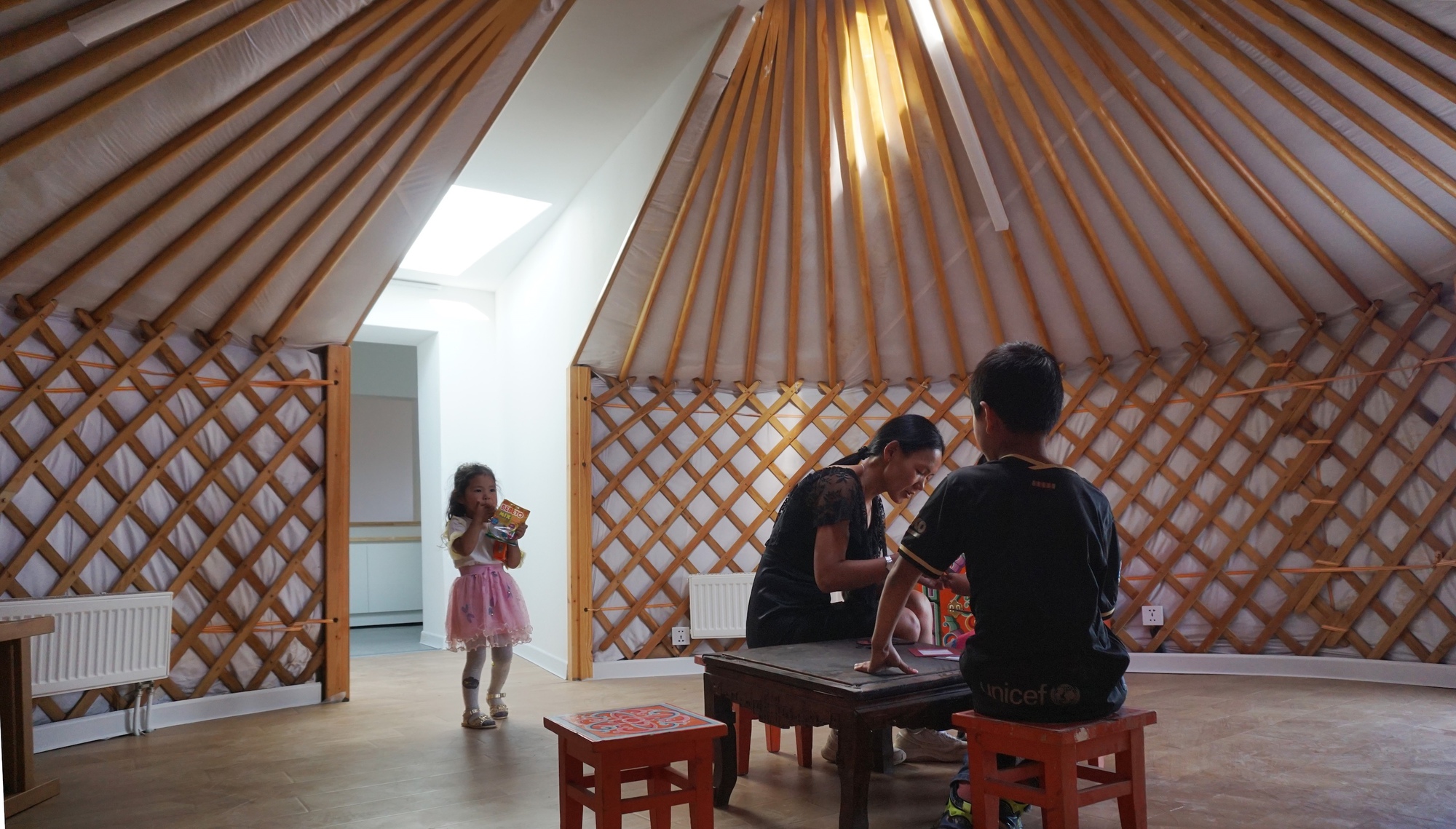 Interior of the yurt showing radial timber roof beams and lattice walls with a family gathered inside