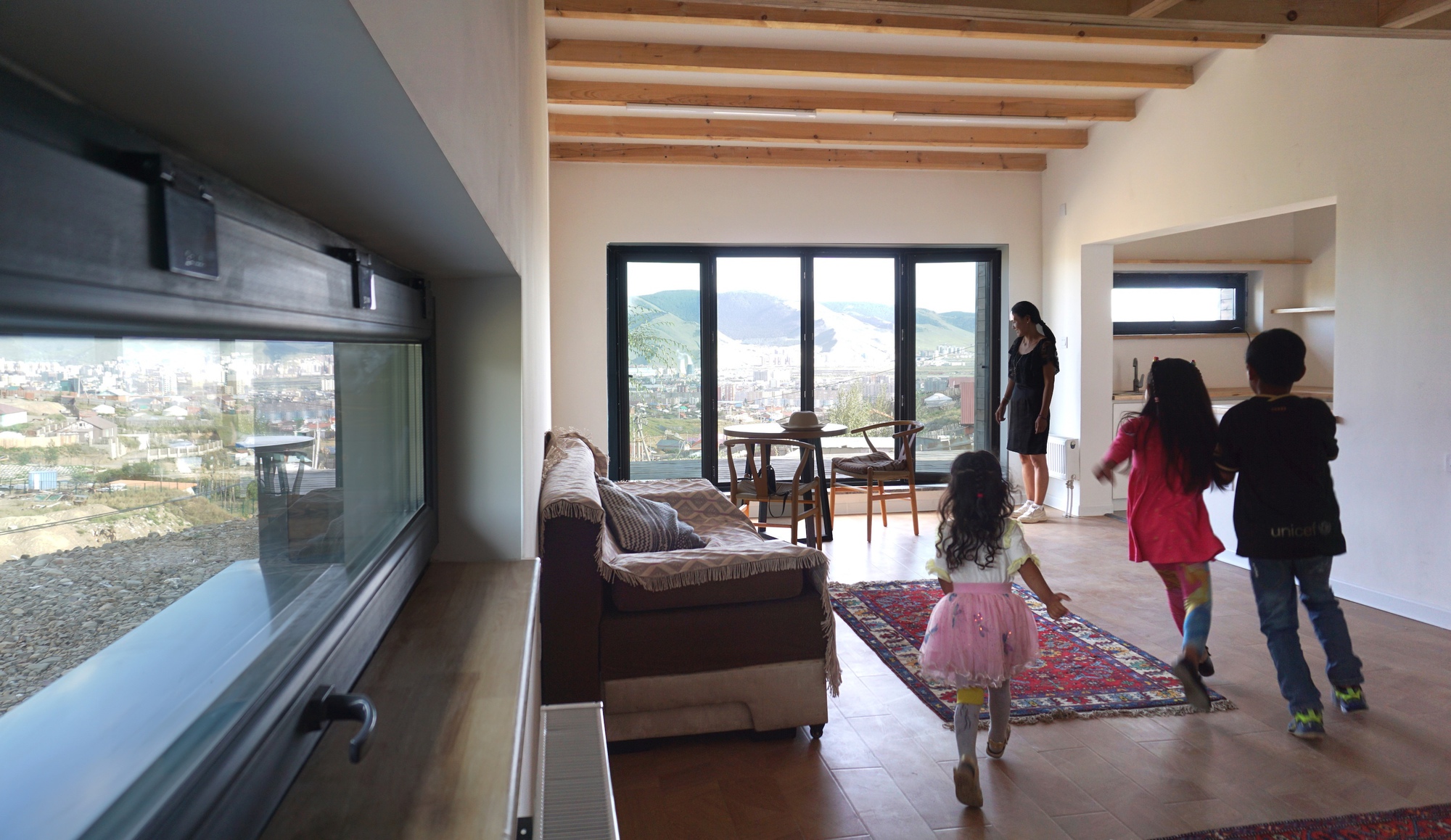 Living space with horizontal window framing the valley below and children playing on a patterned rug