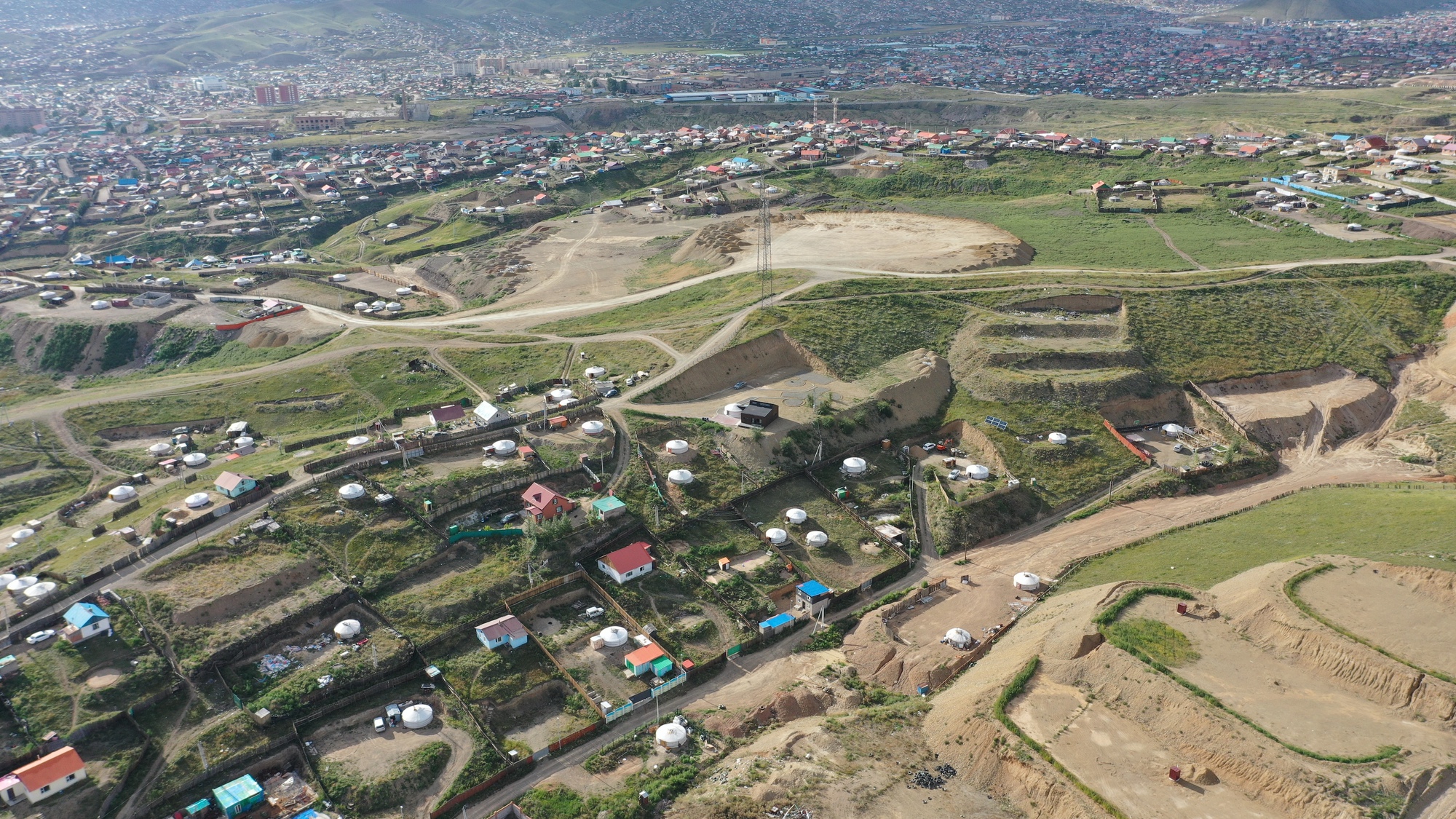 Aerial view of a residential settlement with dirt roads and cultivated plots along a hillside