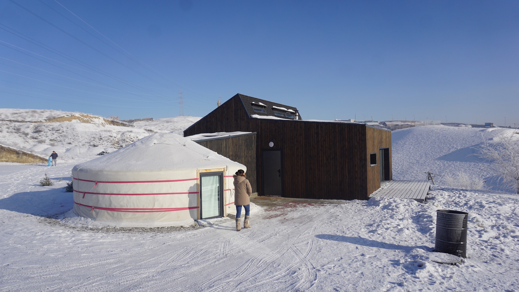 Dark timber-clad volume adjoining a circular yurt structure in a snow-covered landscape