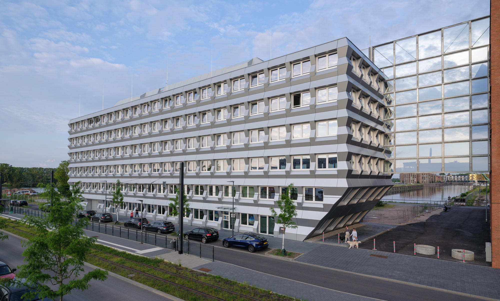 Street view of the repetitive window facade with young street trees and parked cars below