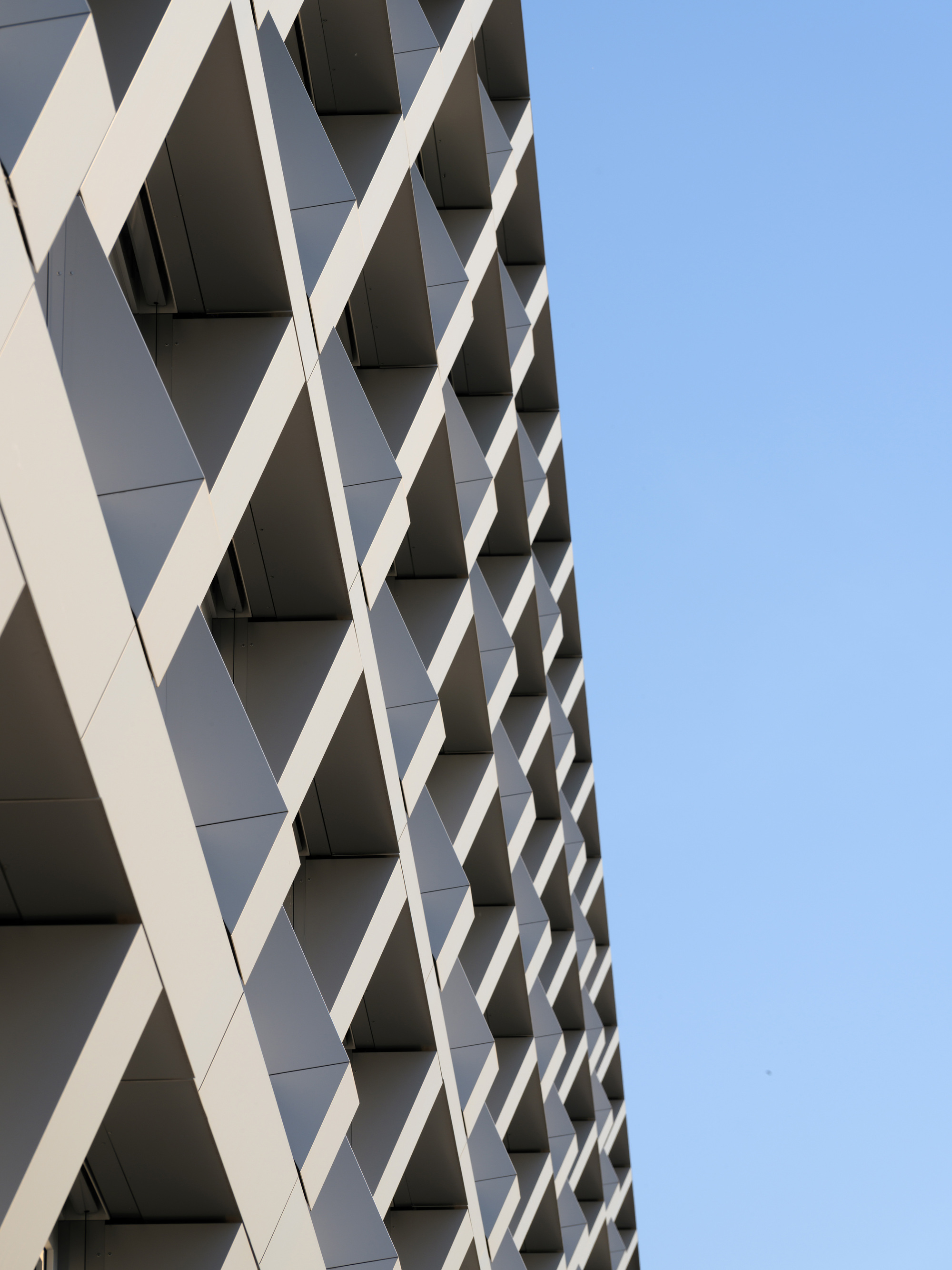 Angled view of the crisscrossing white facade fins creating a diamond pattern against clear blue sky