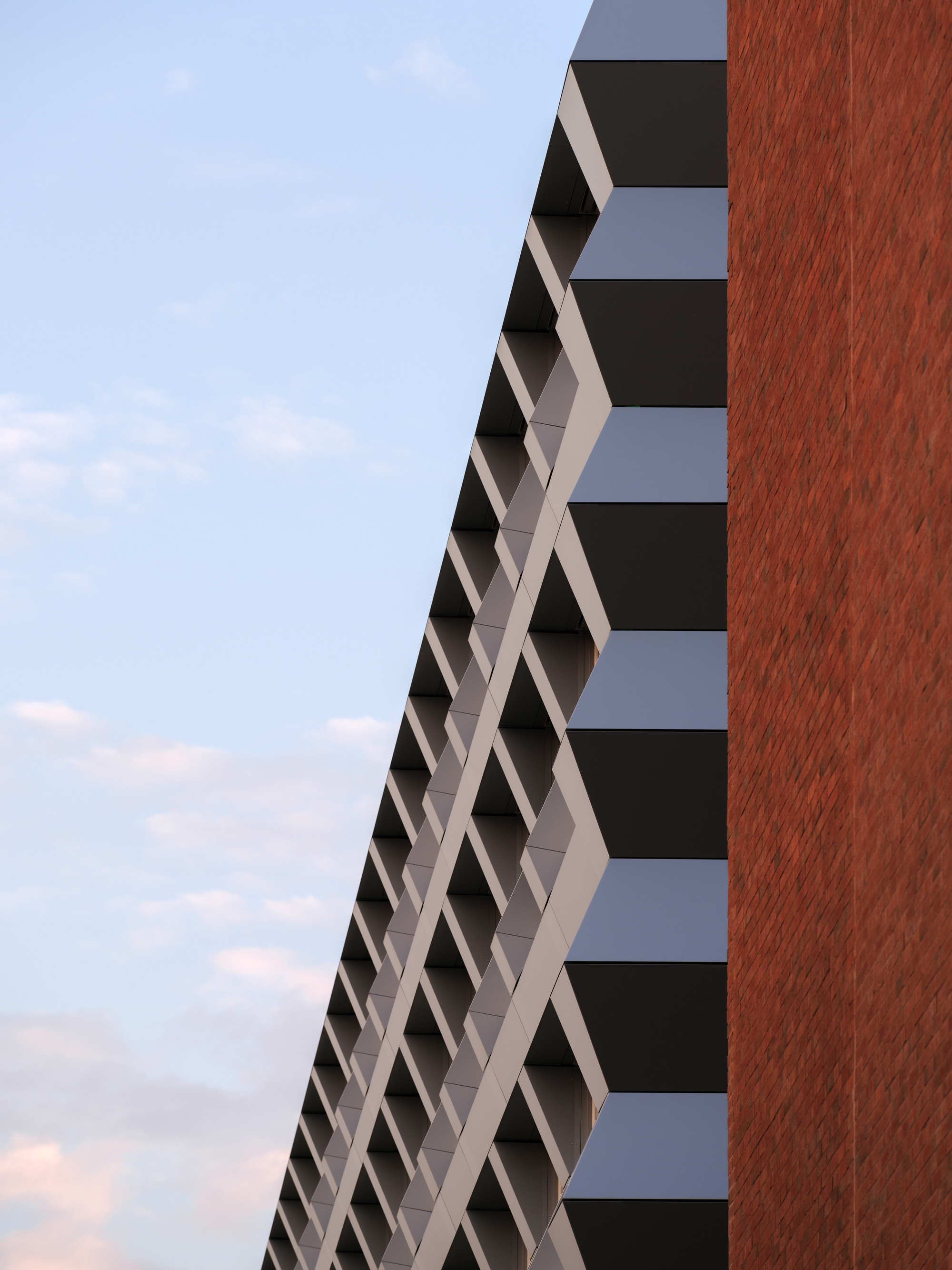 Diagonal facade with white sunshading elements meeting the vertical red brick tower volume at dusk