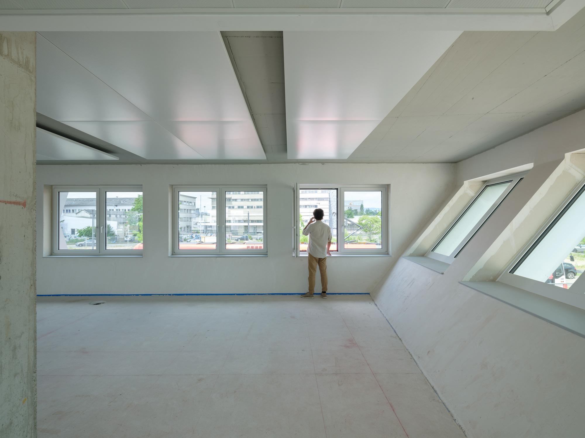 Interior with angled skylight and windows where a person stands gazing at the urban view