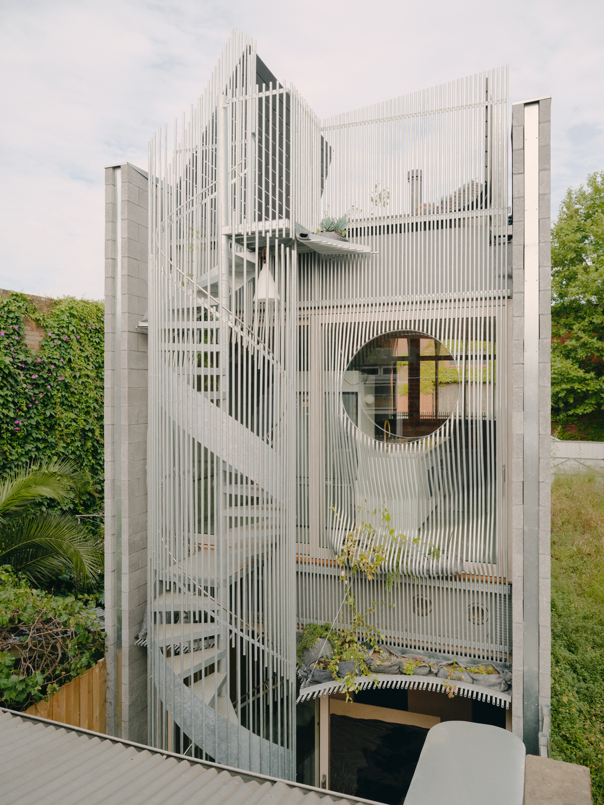 Facade detail showing vertical metal slats wrapping the curved form with circular window and exterior stair