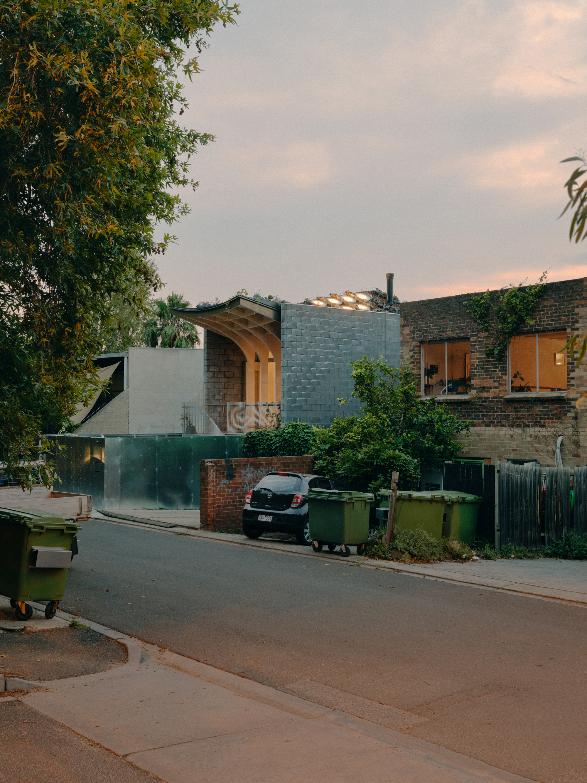 Evening streetscape showing the curved roof and concrete block volume between brick neighboring houses