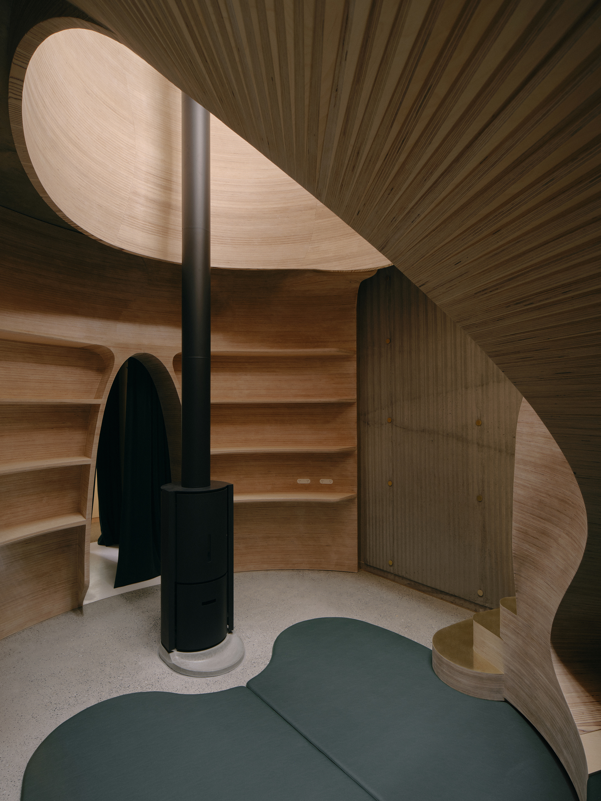 Curved timber interior space with black stove column and ribbed ceiling meeting organic timber walls