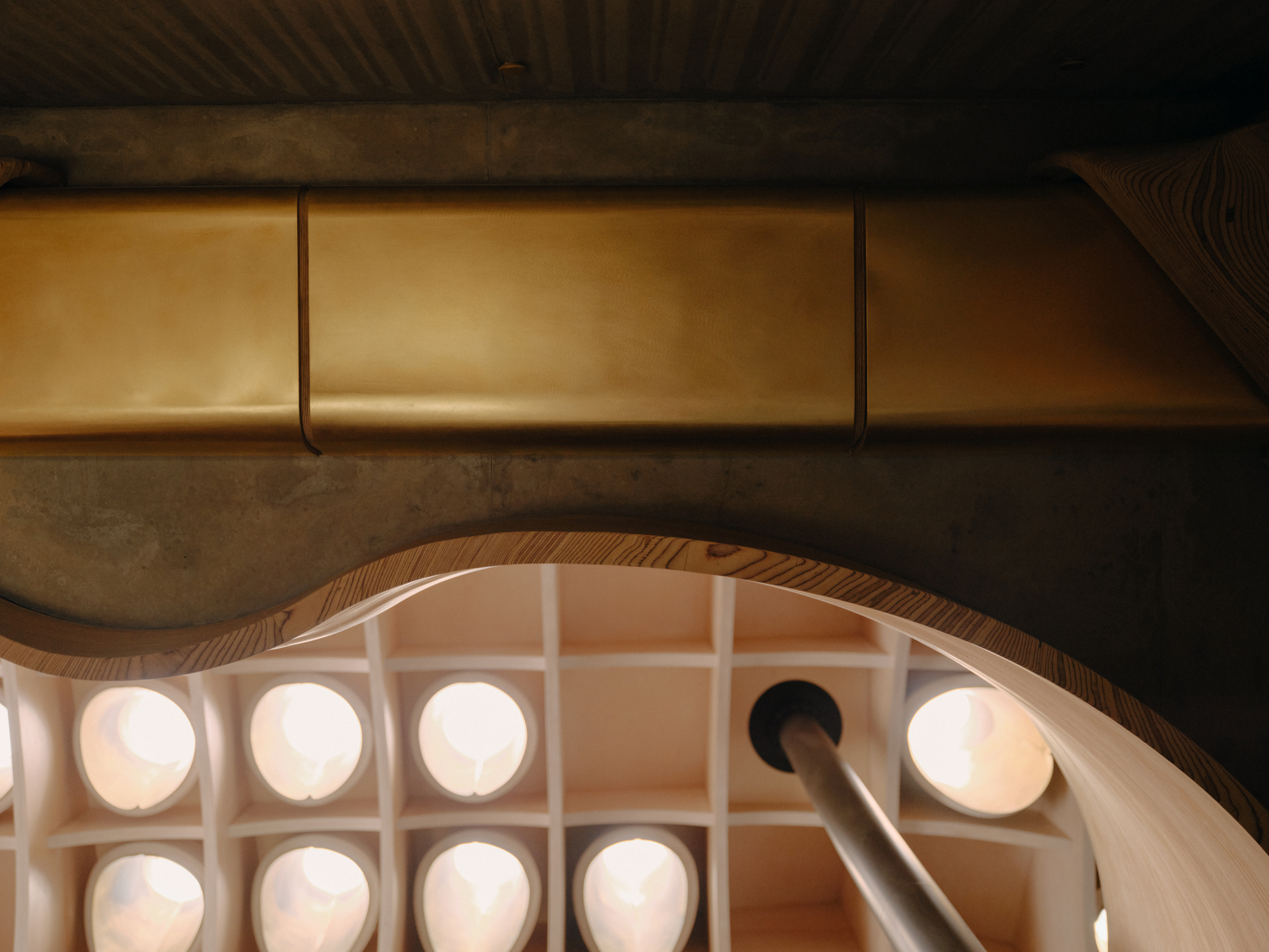 View down into the oval stairwell showing circular skylights and a metal handrail piercing the opening