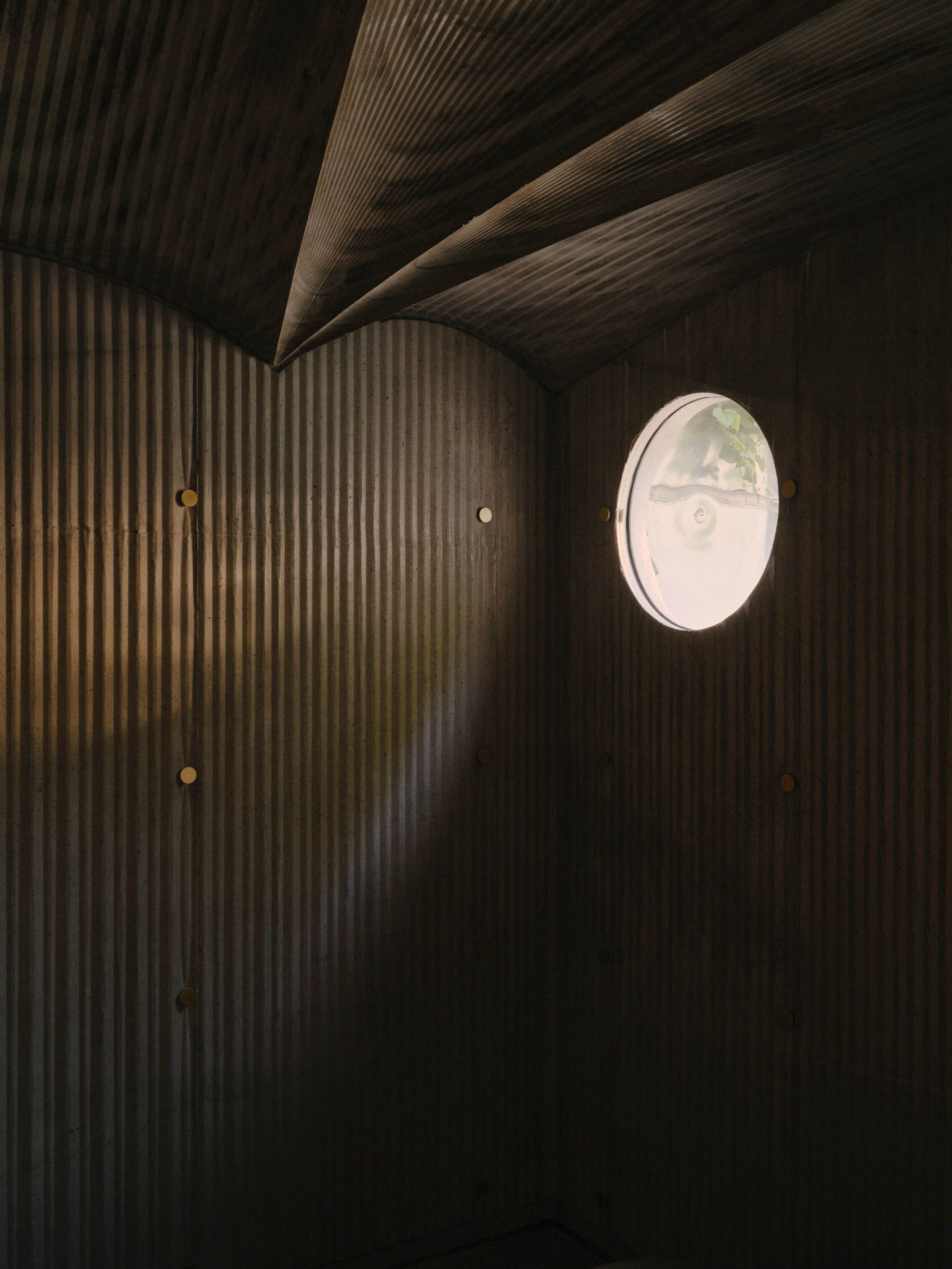 Dark timber slatted wall and ceiling meeting at an angled corner with a single round window