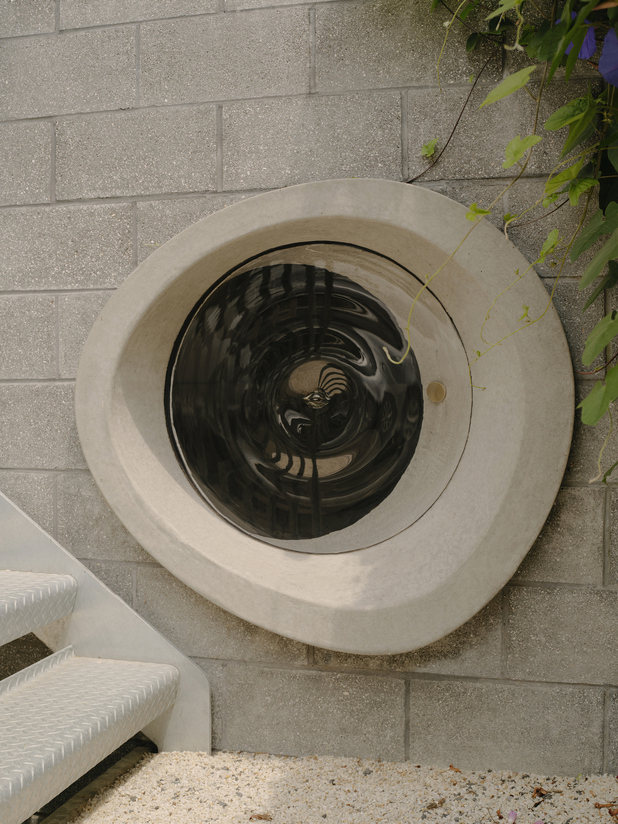Overhead view of a circular skylight set into a concrete frame on a paved terrace with foliage