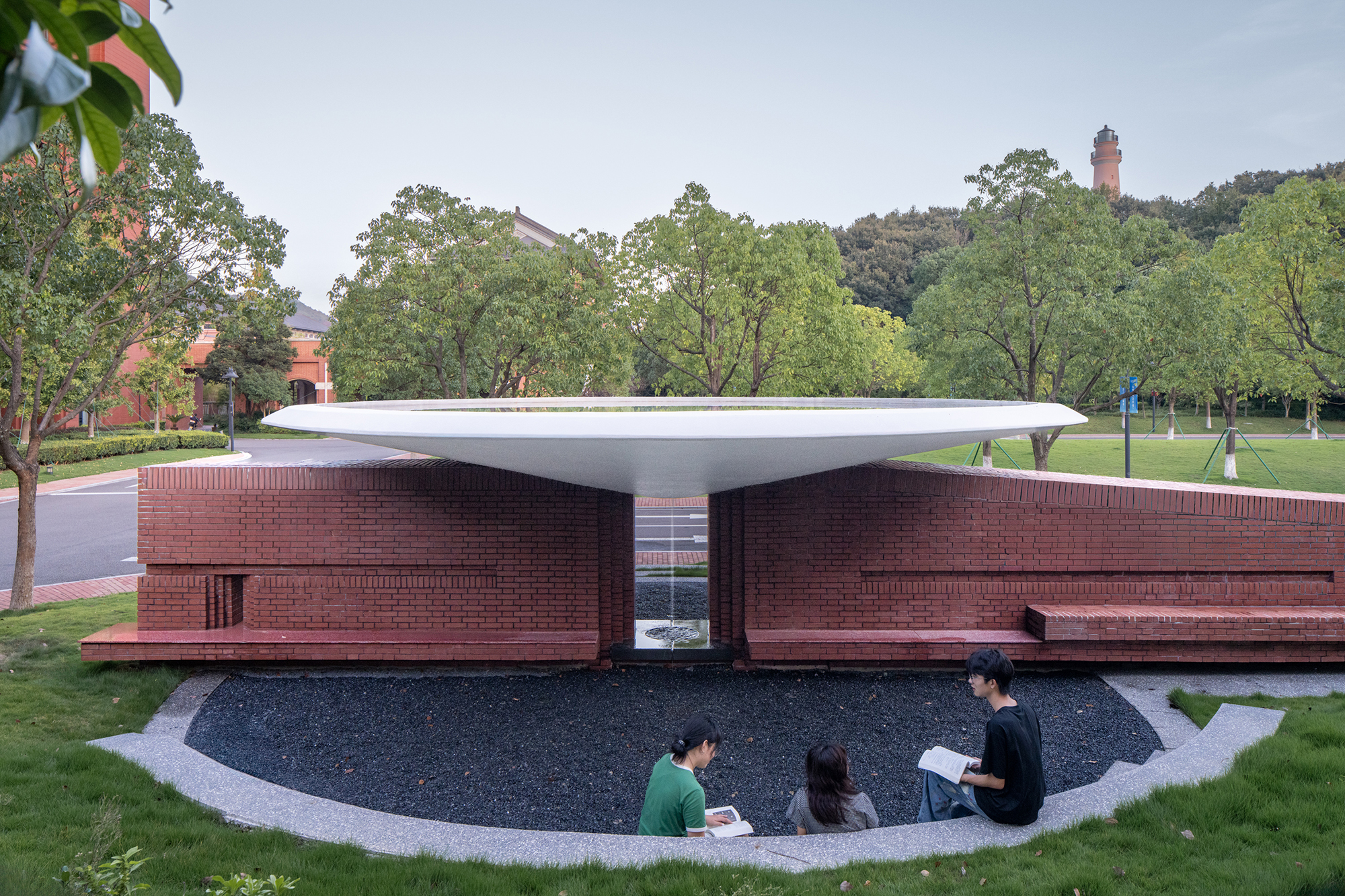 Pavilion with thin white canopy sheltering brick walls and a sunken courtyard where students sit reading