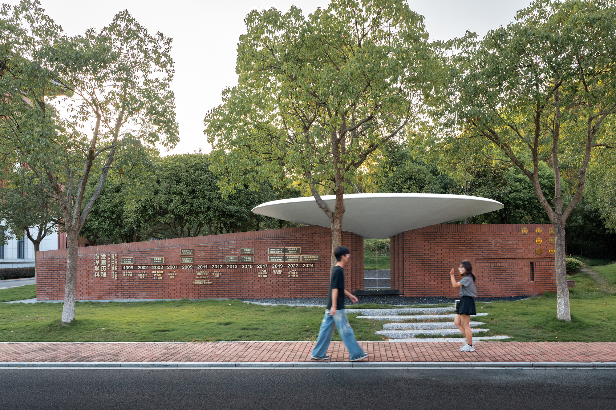 Street view of the brick memorial wall with inscribed names beneath the canopy and pedestrians passing