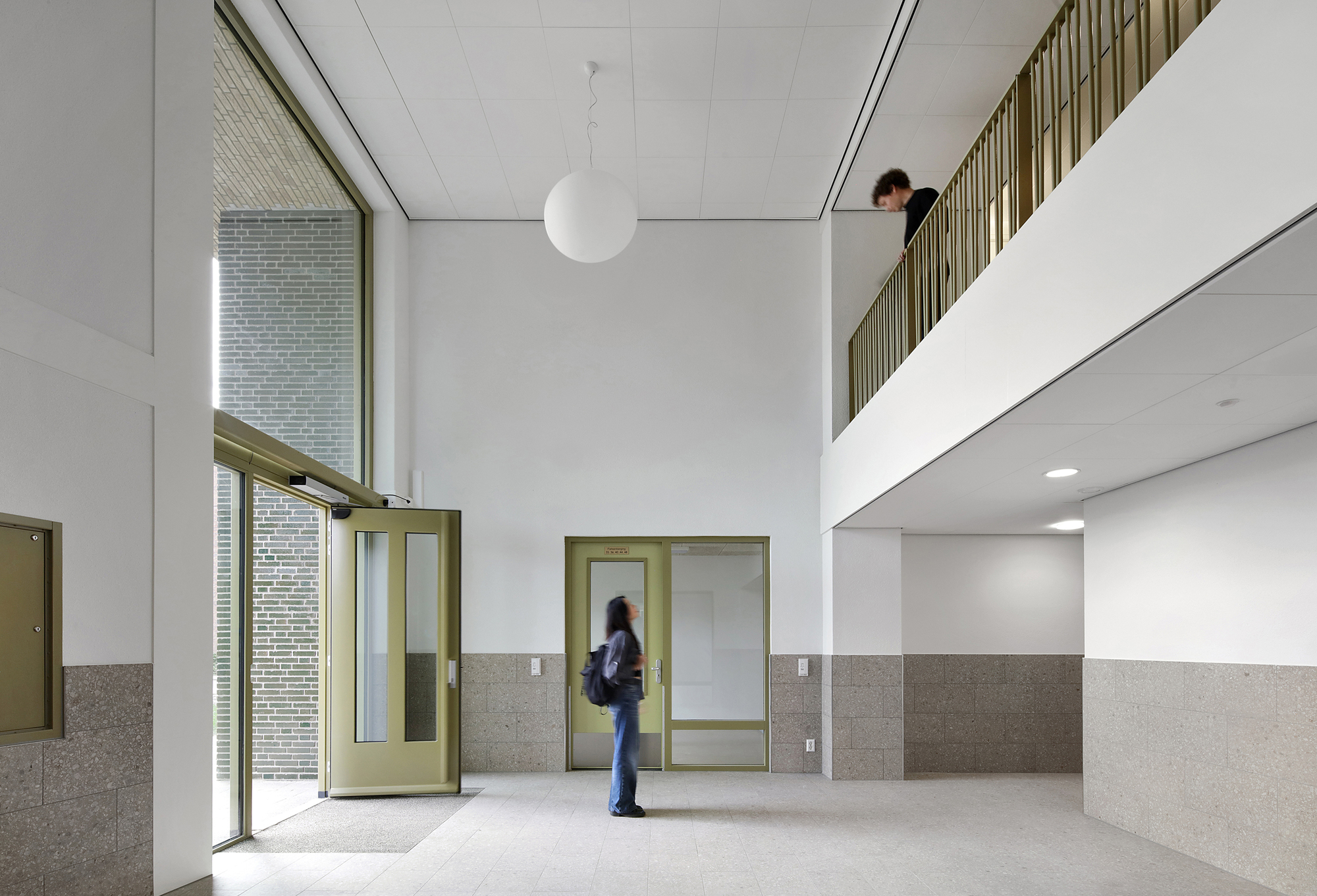 Double-height entrance lobby with terrazzo wainscoting, green metal door frames, and a mezzanine above