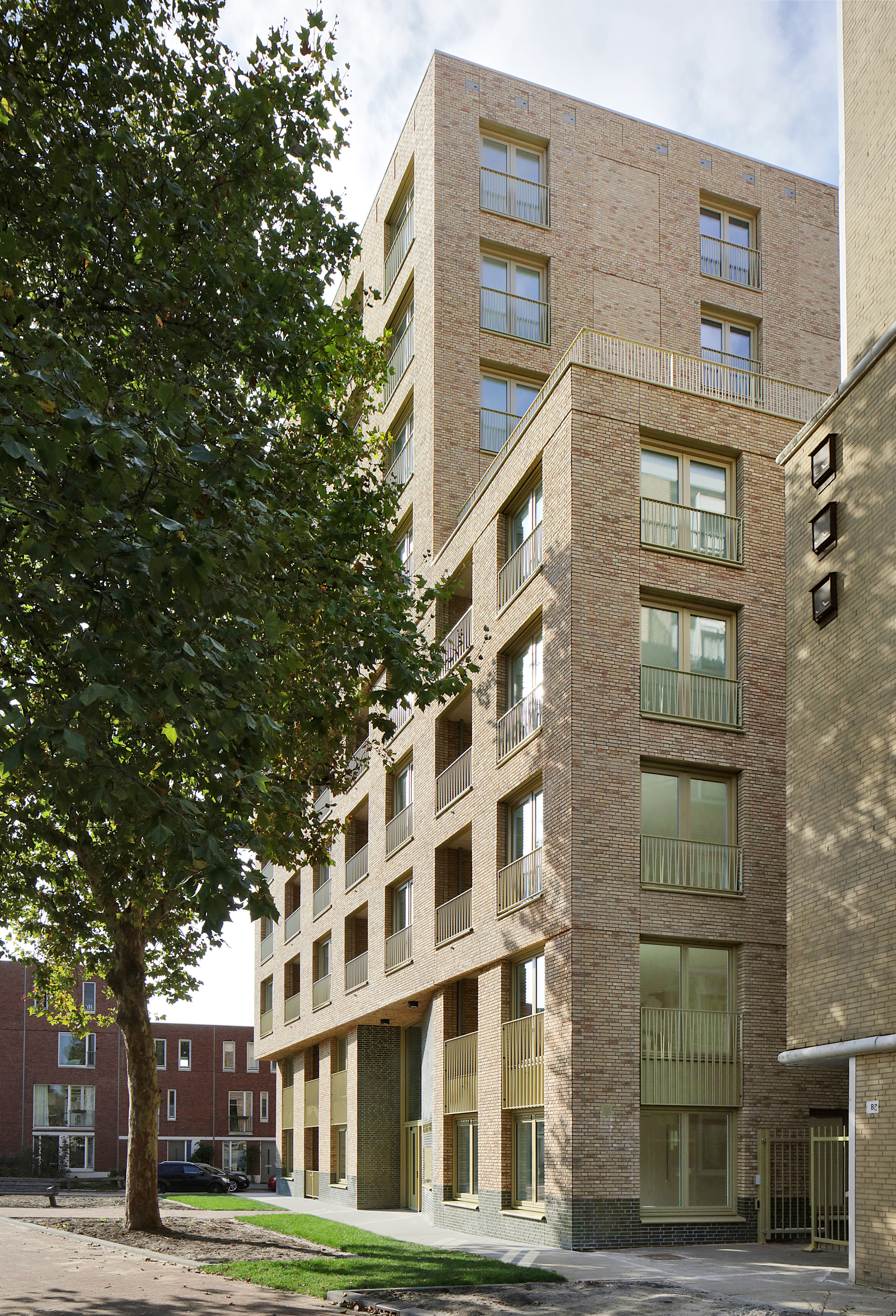 Street elevation of a buff brick housing block framed by mature trees in summer foliage