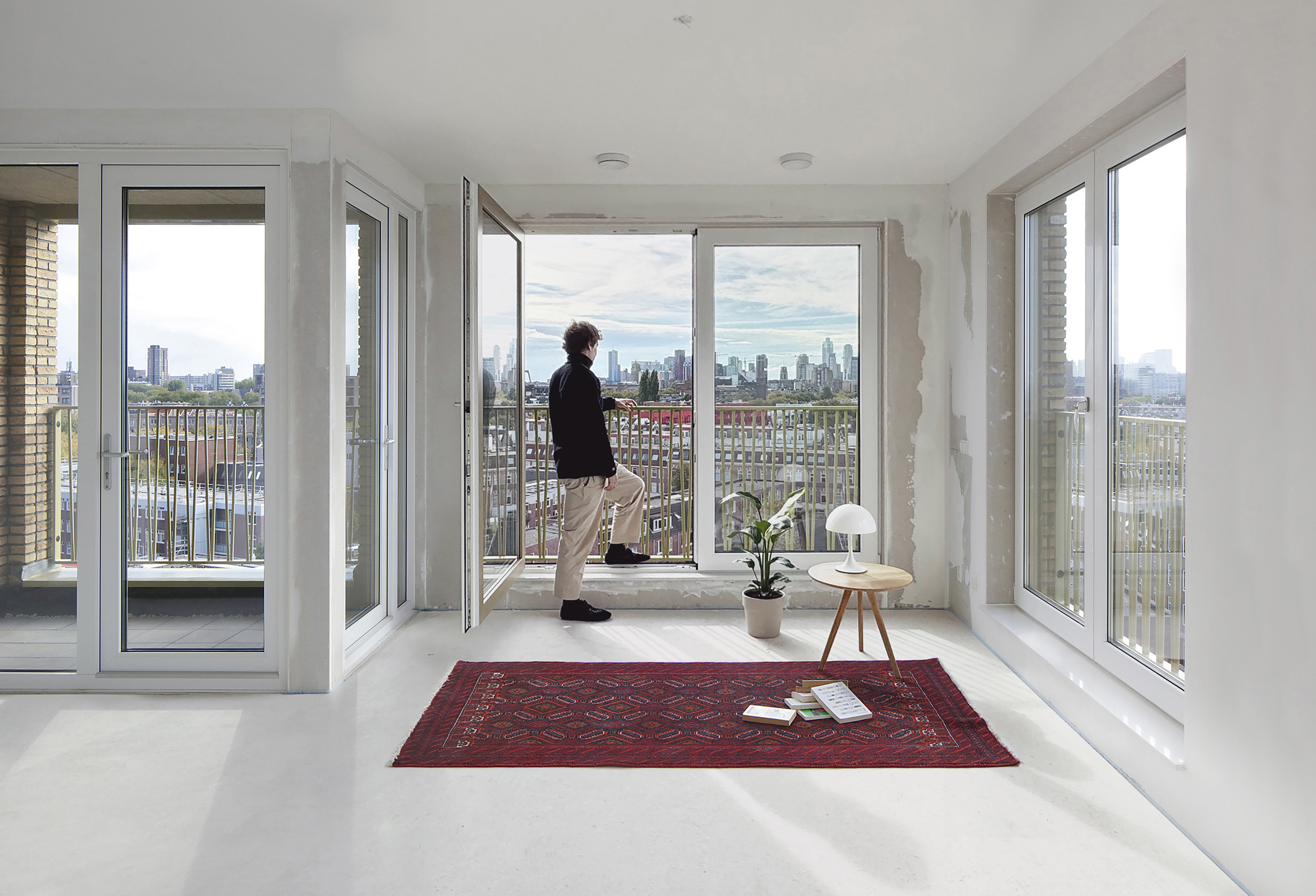 White interior room with floor-to-ceiling windows opening to a balcony overlooking the cityscape