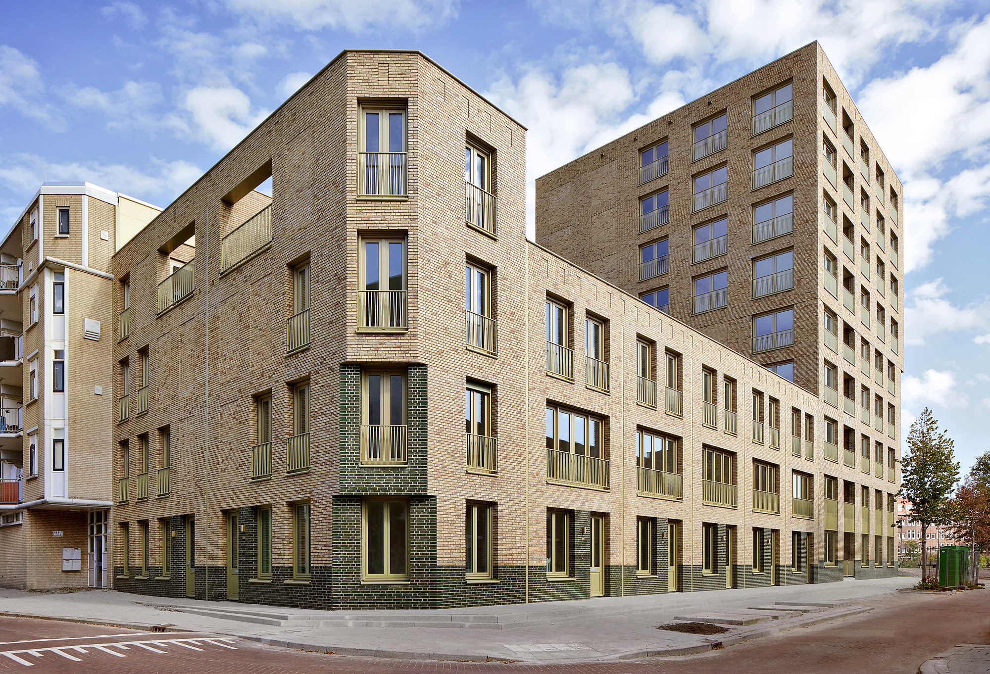Street corner view of the buff brick facade with punched windows and green tile accents