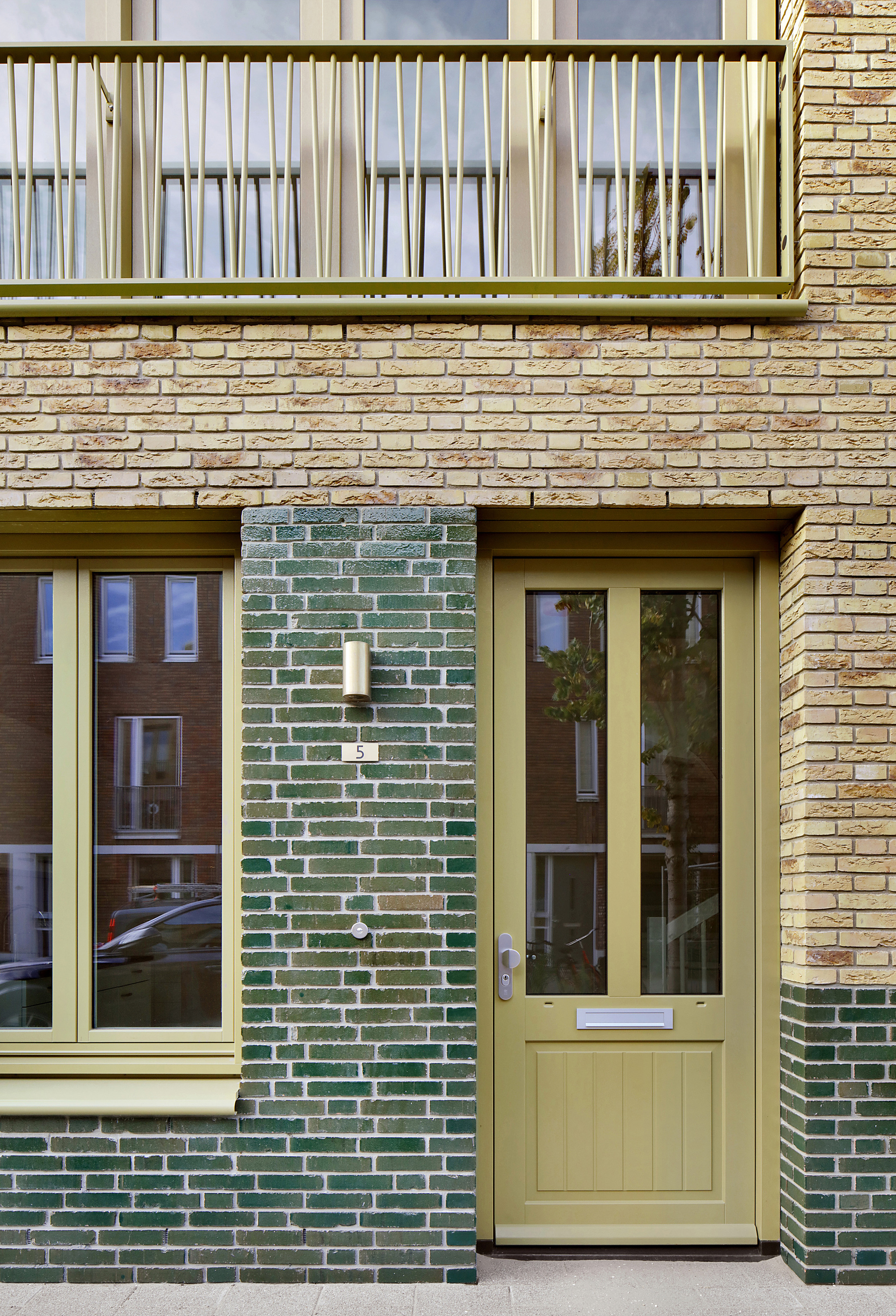 Ground floor entrance with pale yellow door framed by green glazed brick and buff brick