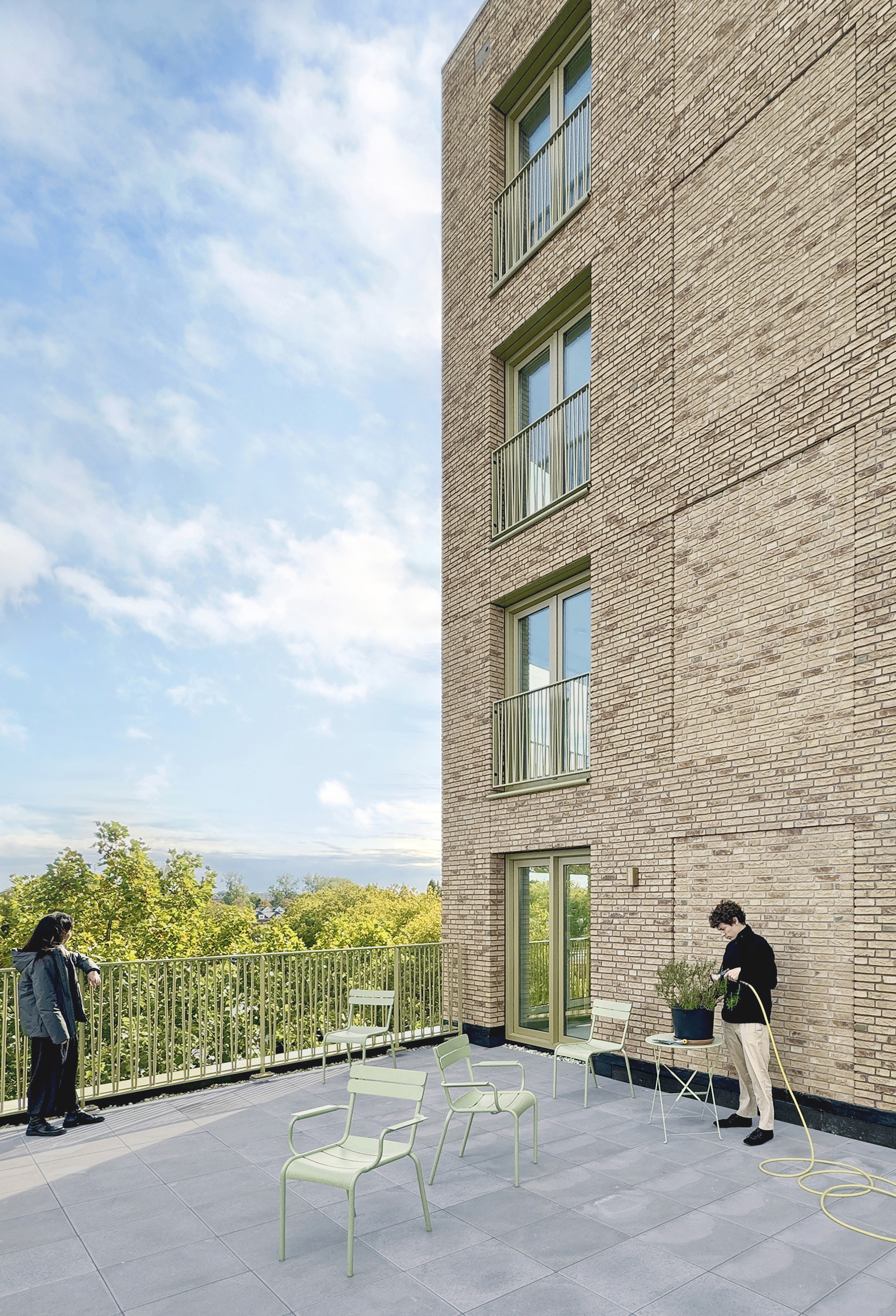 Shared terrace against the brick tower with pale green chairs and residents in afternoon light