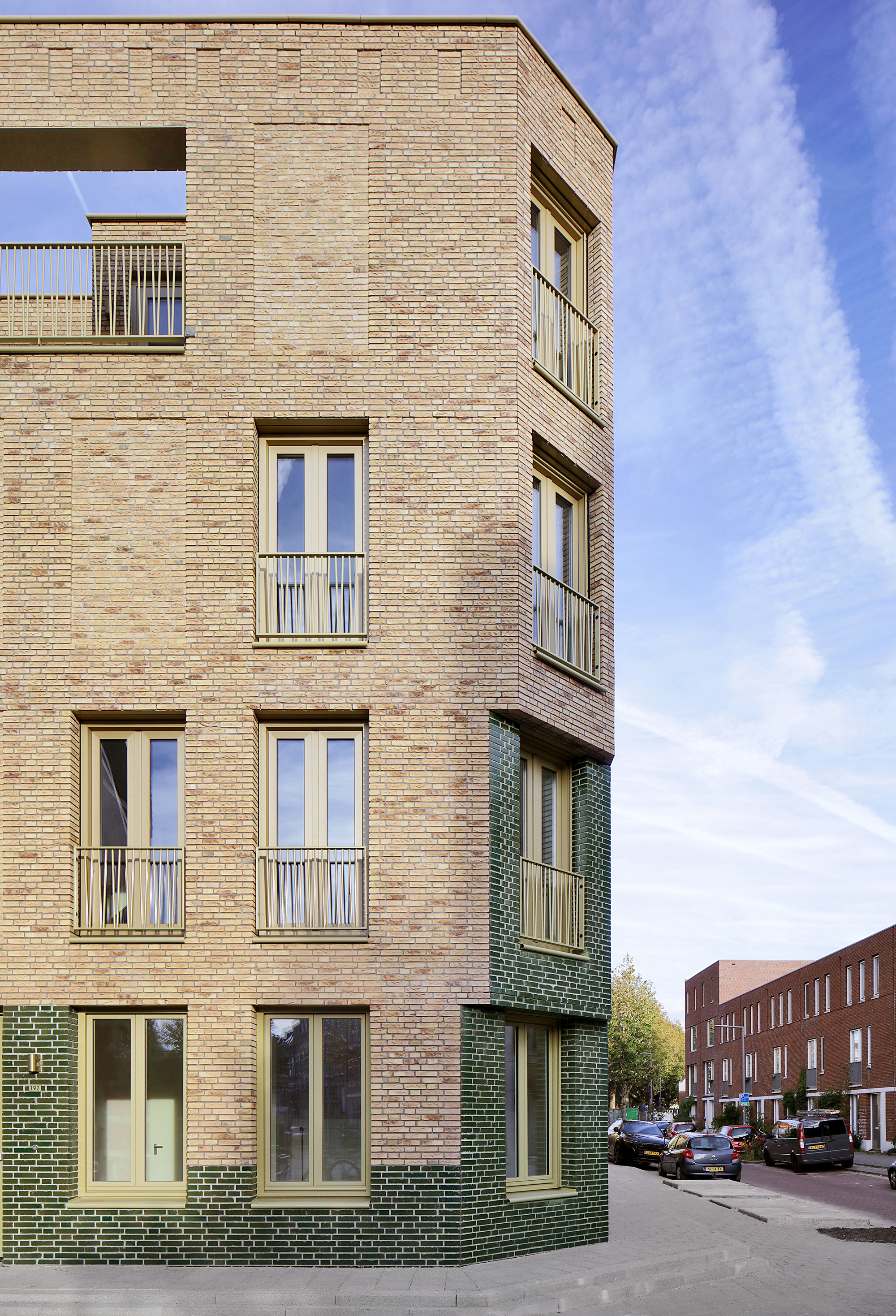 Corner detail showing the alternating buff and green brick cladding under a partly cloudy sky