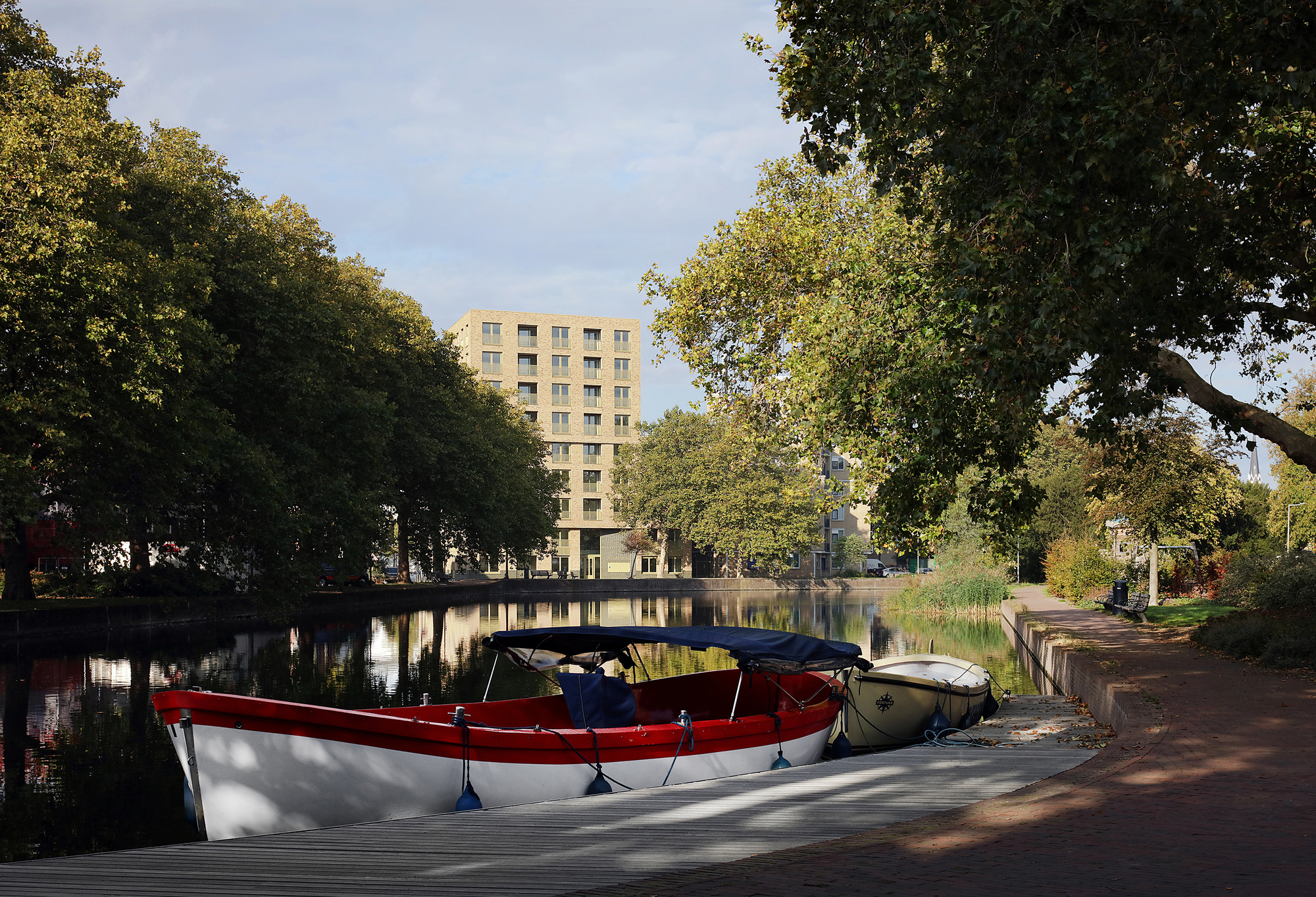 Residential tower viewed across a canal with moored boats and overhanging tree branches