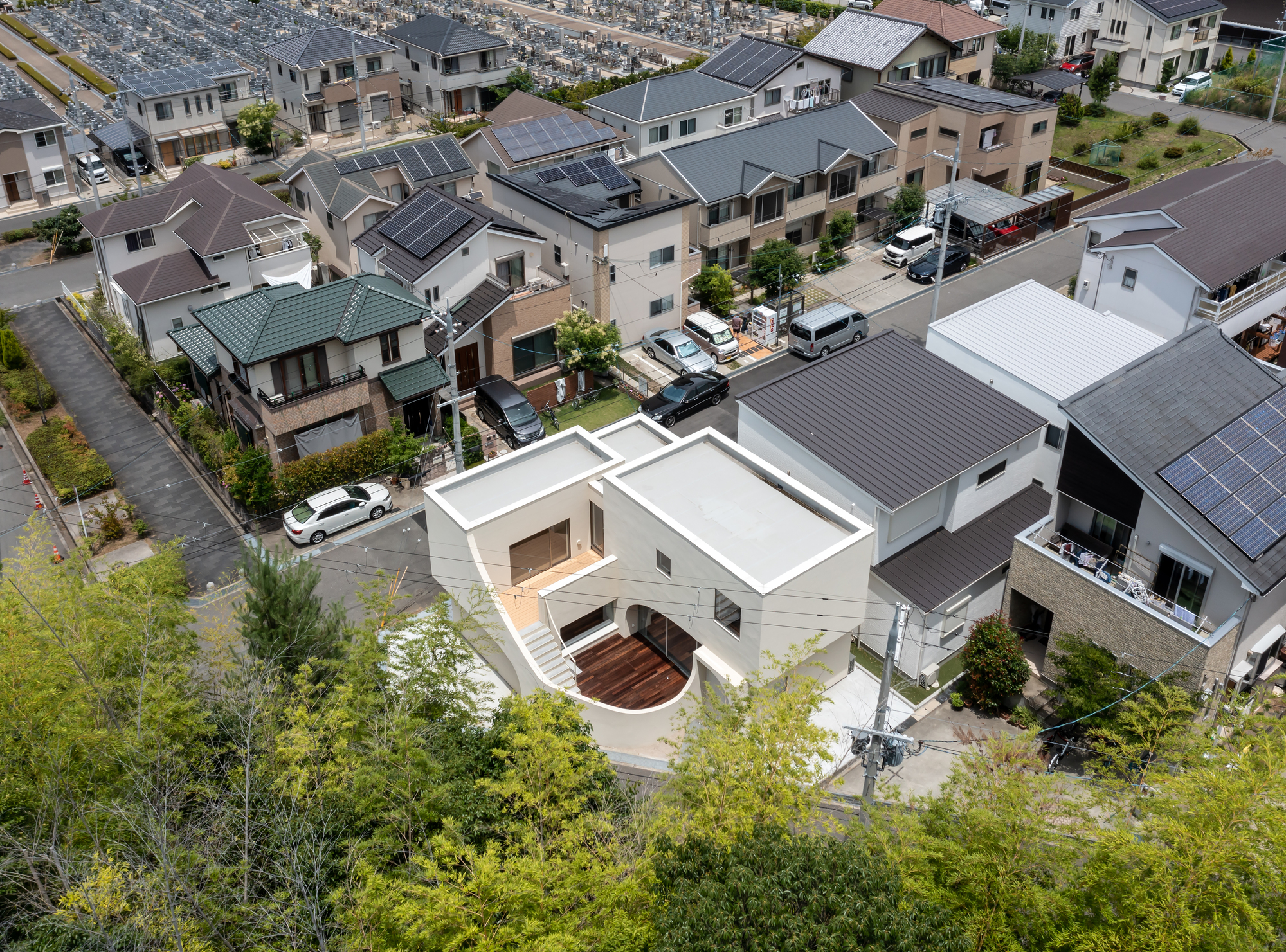 Aerial view of white rooftop with curved courtyard and timber deck nestled within a dense suburban neighborhood