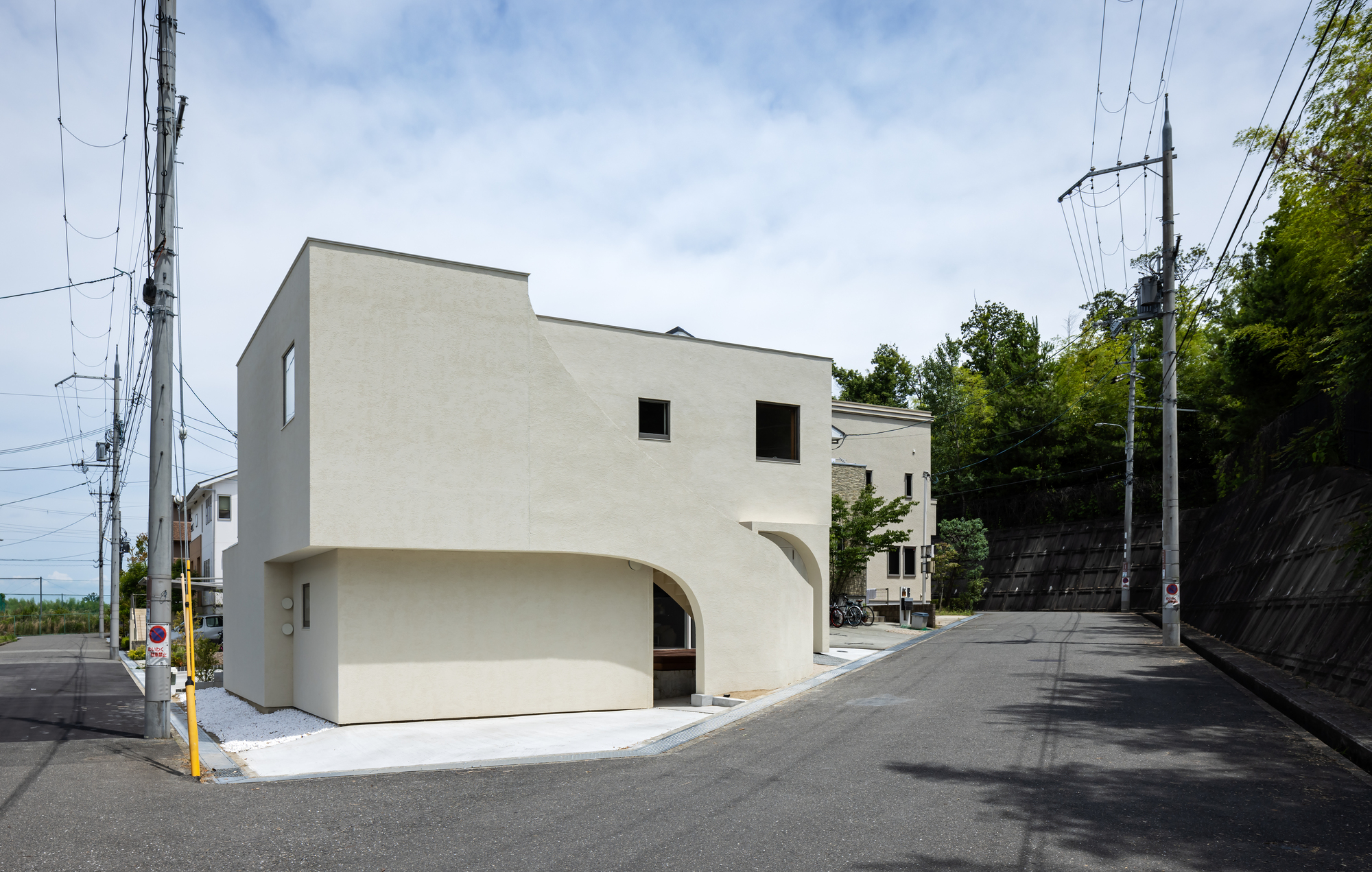 Corner facade with arched recesses at the base and punched square windows above on a sloped street