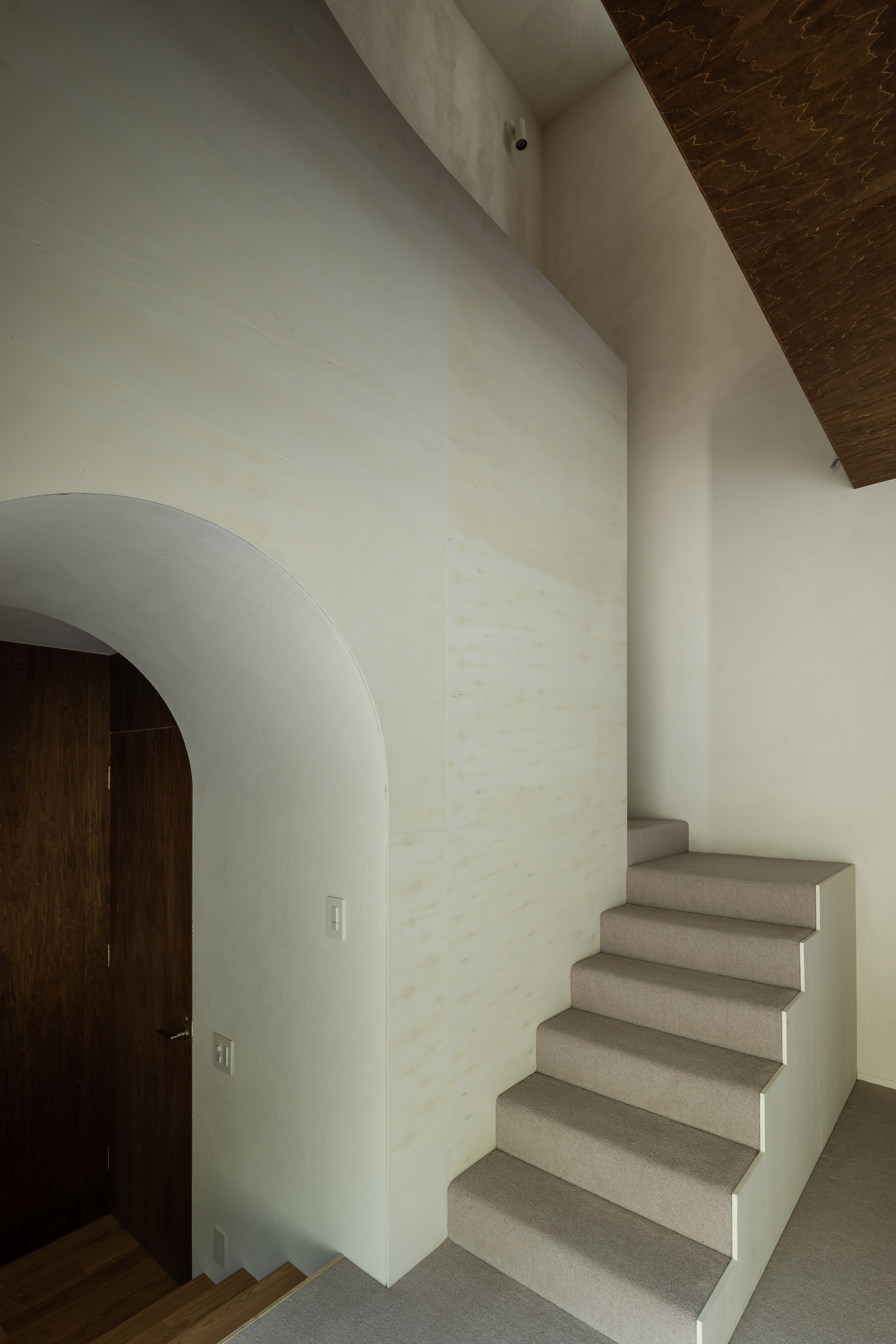 Interior staircase with pale terrazzo treads rising alongside a white wall with an arched doorway and timber ceiling