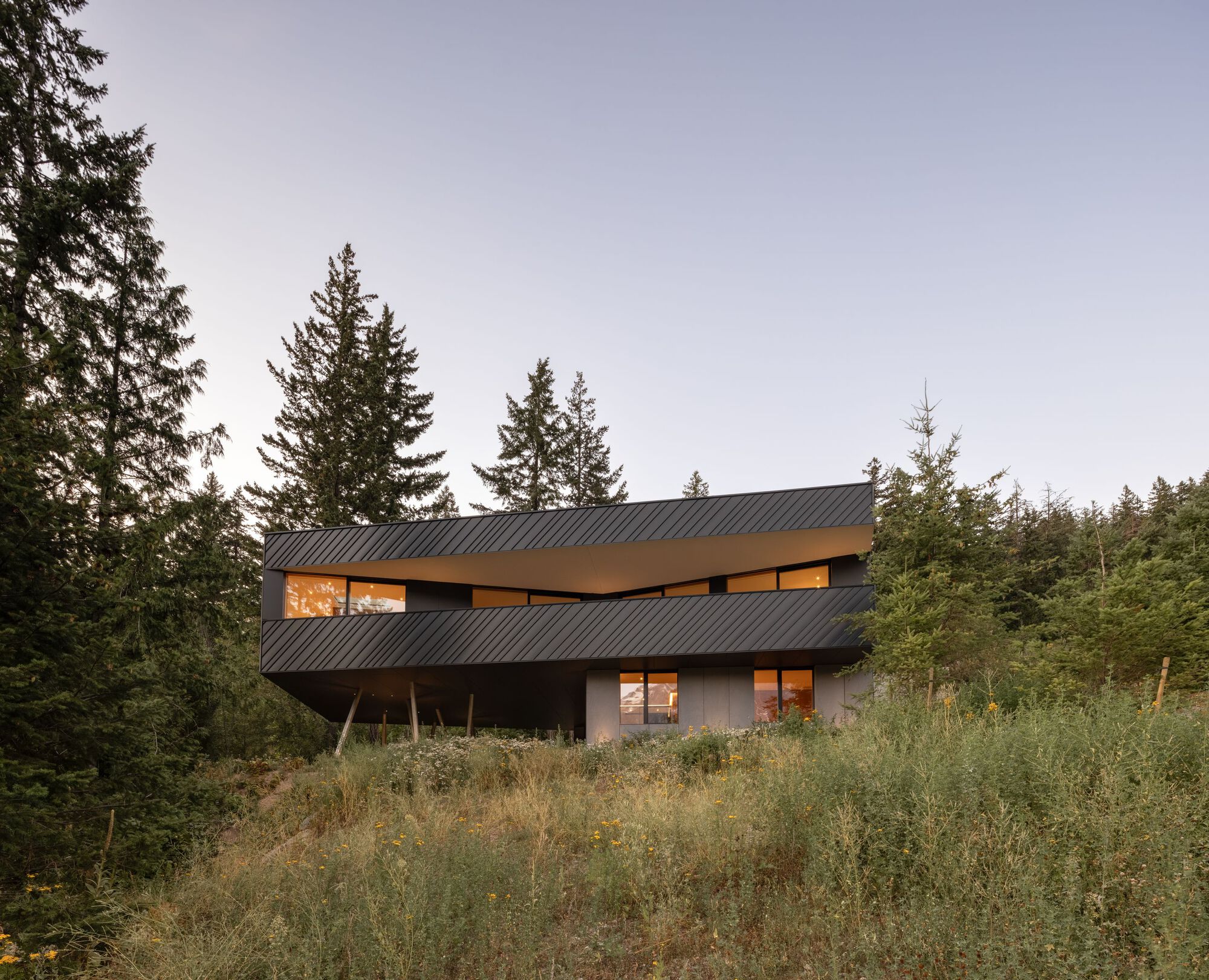 Exterior view of the cantilevered upper level with diagonal metal cladding at dusk with interior lights on