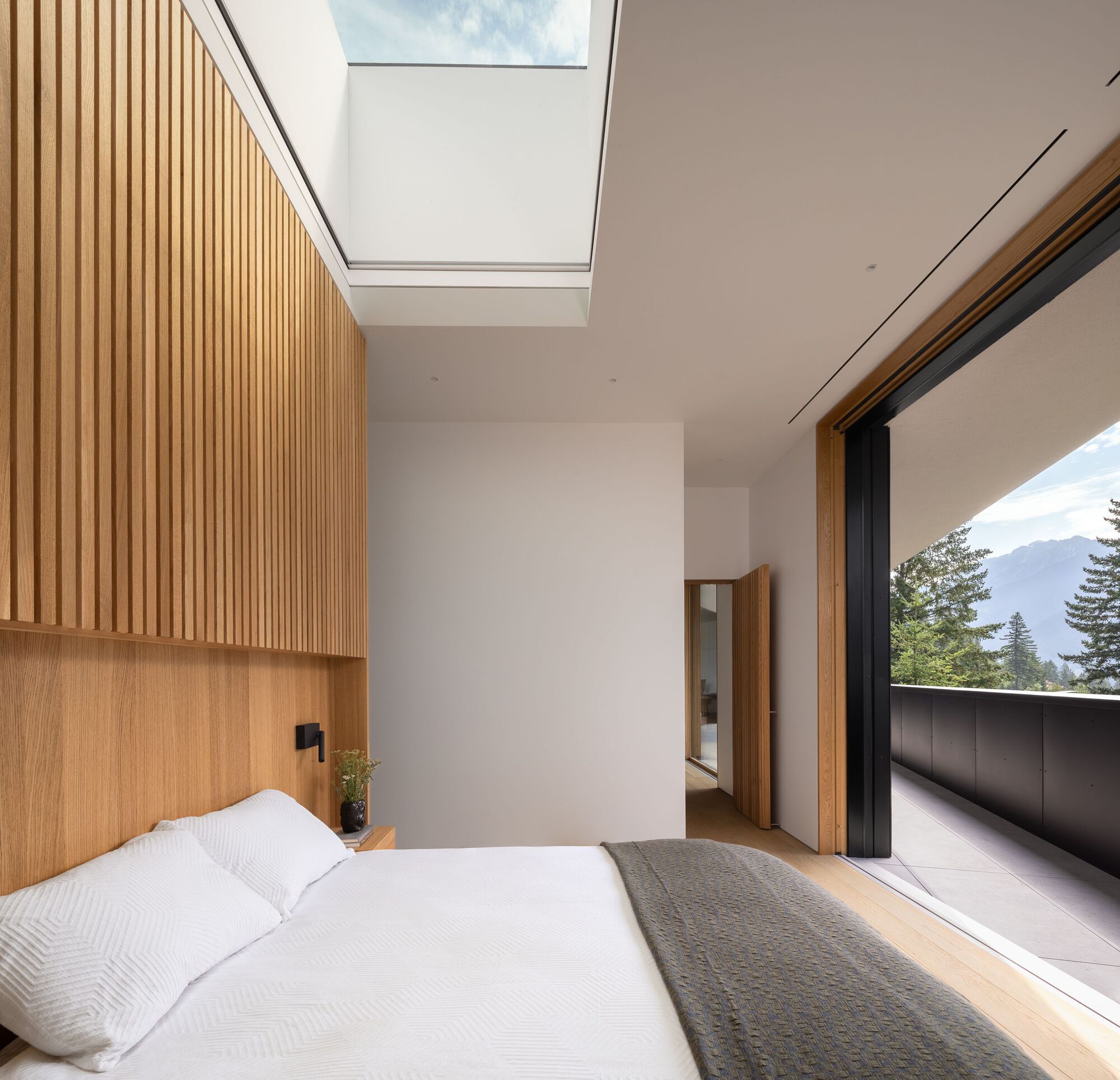 Bedroom with timber slat wall, skylight above, and sliding door opening to a terrace with mountain backdrop