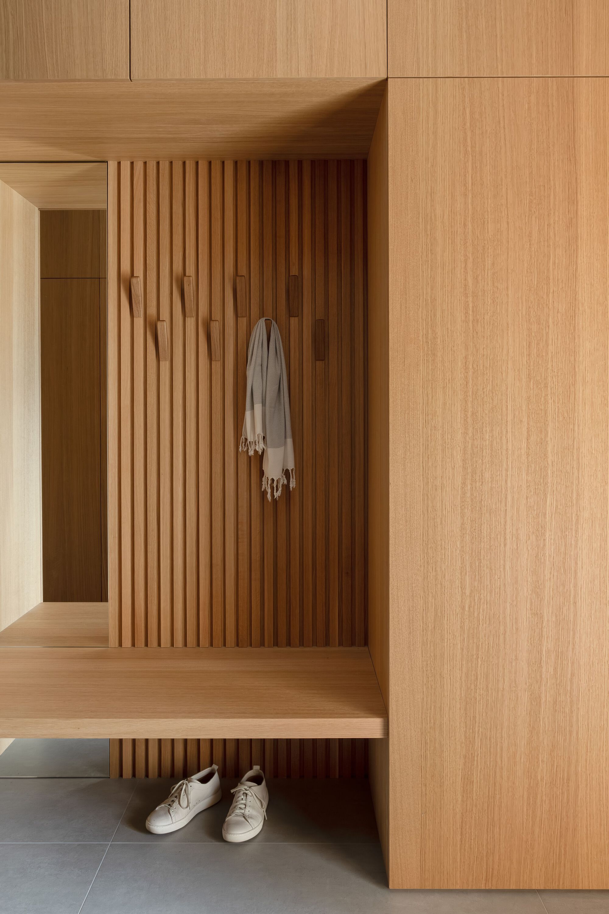 Entryway nook with vertical timber slats, built-in bench and shoes on the floor below