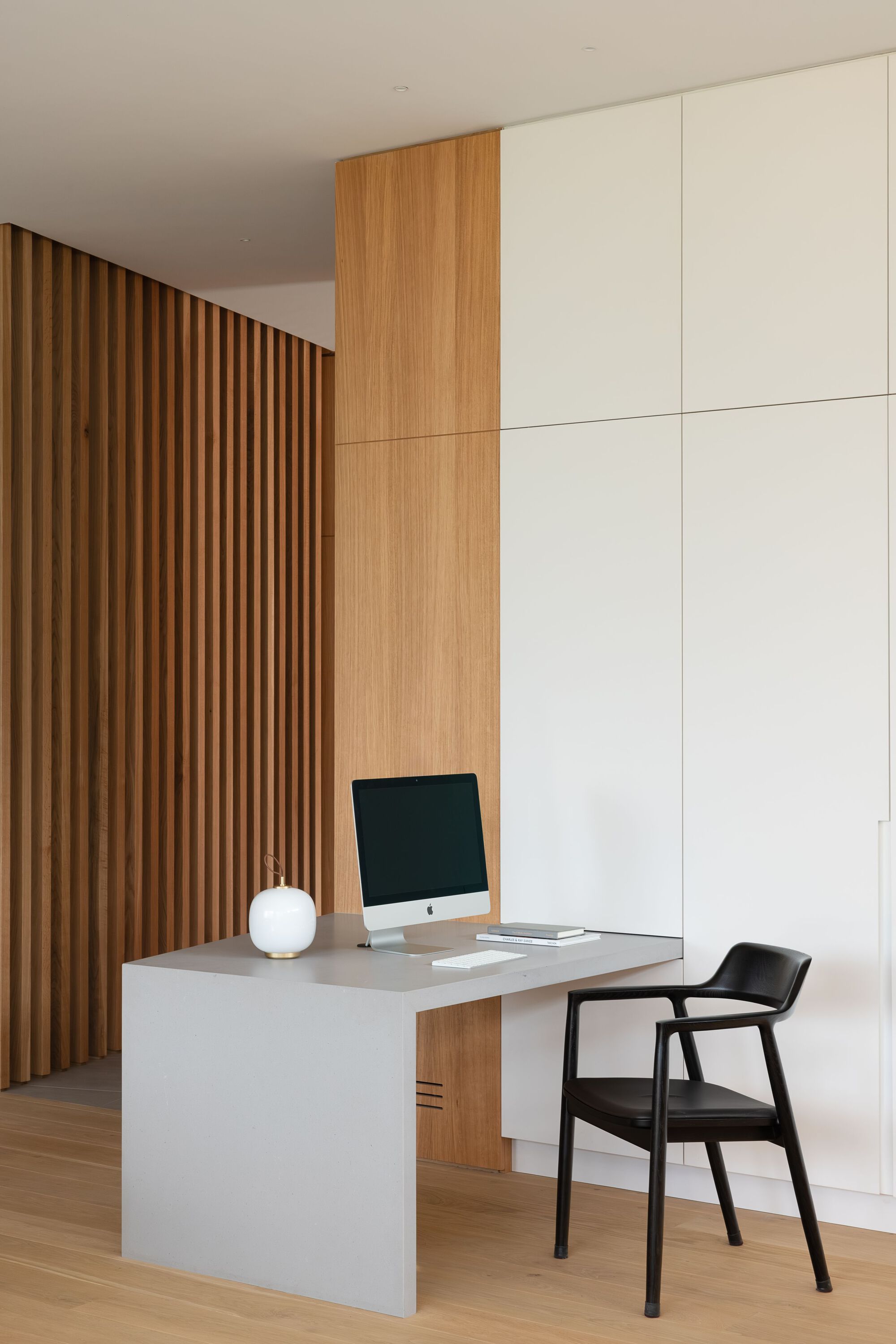Interior workspace with vertical timber slat wall and white storage cabinets above a pale desk