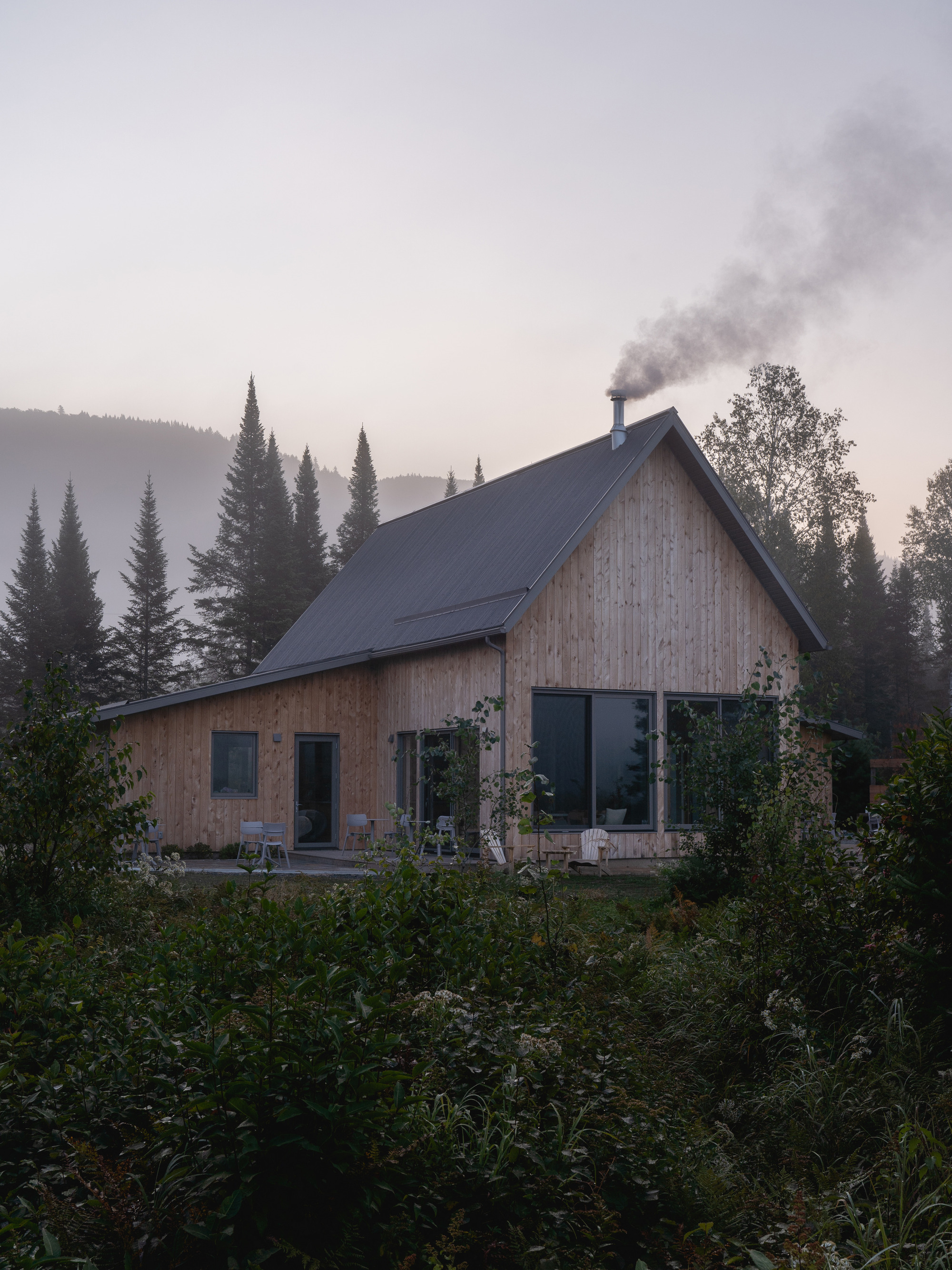 Timber-clad gable roof cabin with chimney smoke rising into the misty mountain forest at dawn