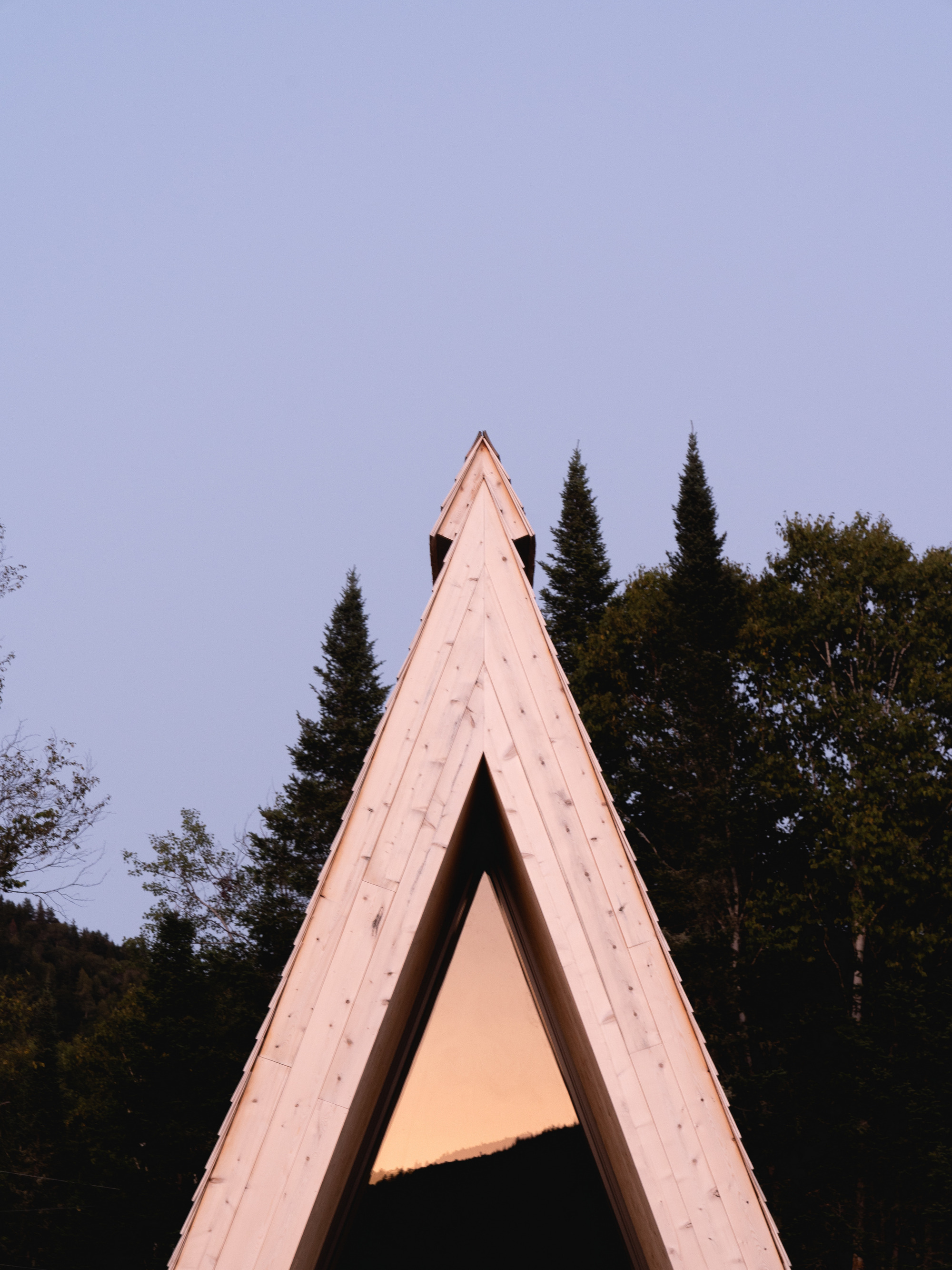 Tall triangular timber frame portal set against dusk sky and darkening conifer treeline