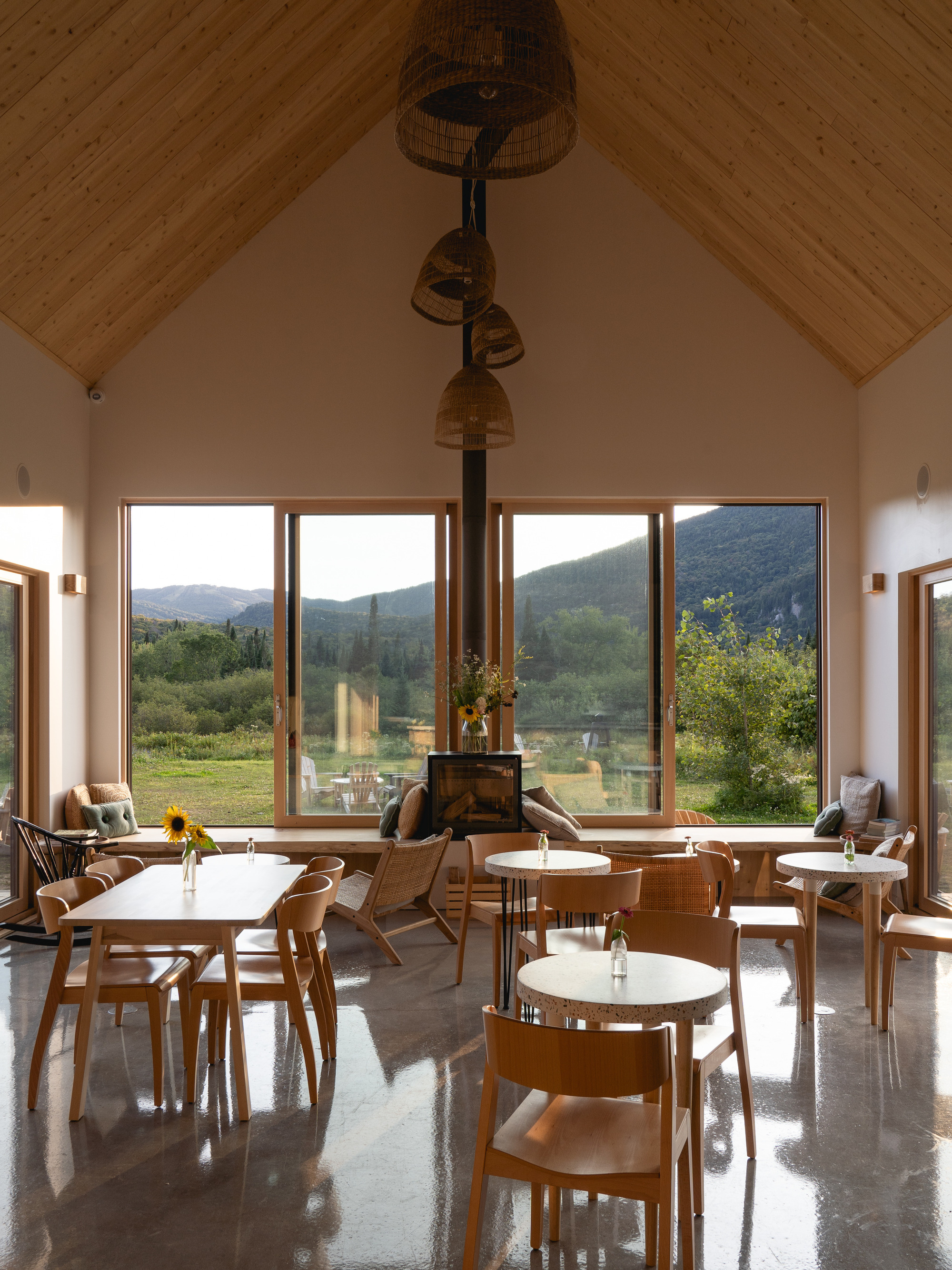 Dining hall interior with vaulted ceiling, timber-framed windows framing mountain views and woven pendant lights