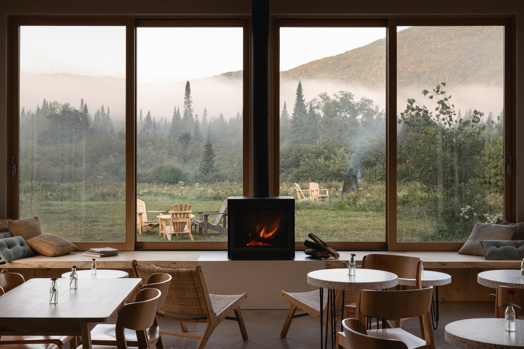 Central woodstove and floor-to-ceiling windows overlooking meadow and forested hills shrouded in morning mist