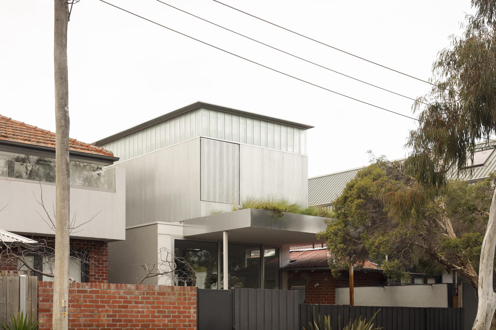 Street view of the two-storey addition with vertical metal cladding above a cantilevered terrace and dark fence