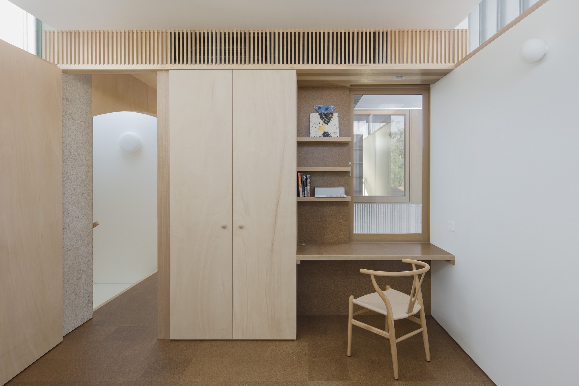 Built-in plywood desk and storage wall with slatted screen above in a compact study nook