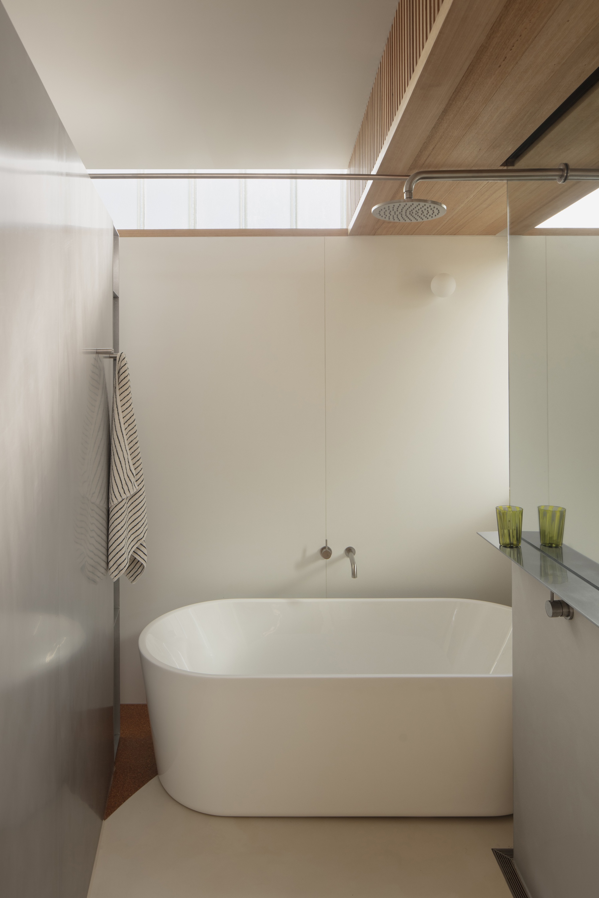 Bathroom with freestanding oval tub beneath a timber-lined soffit and high glazing