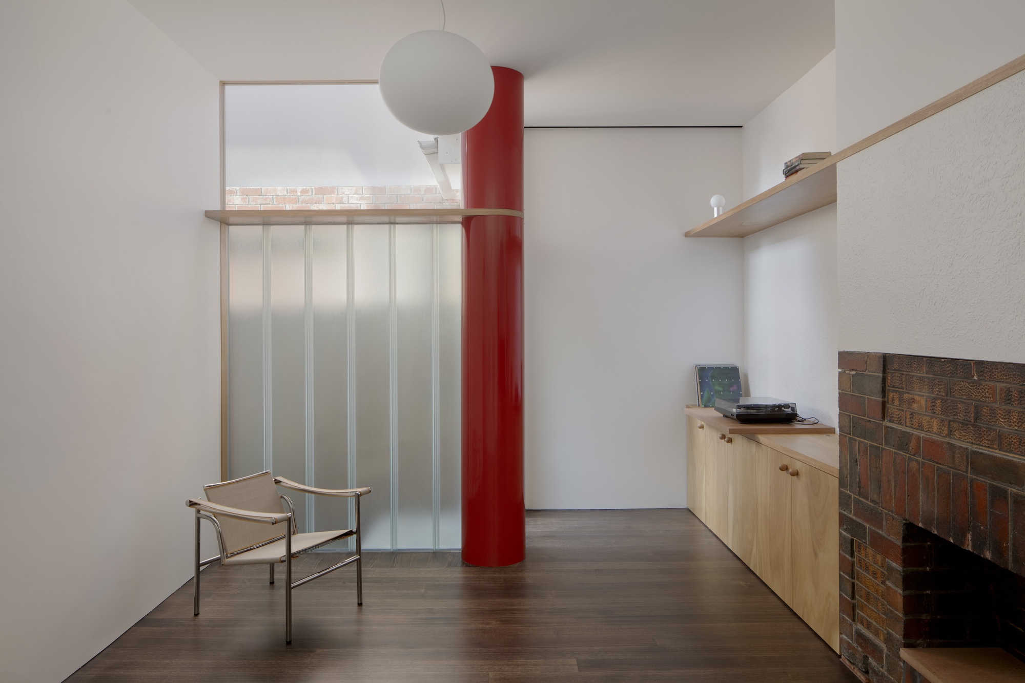 Living room with red cylindrical column, translucent sliding screen and low cabinet beside brick fireplace