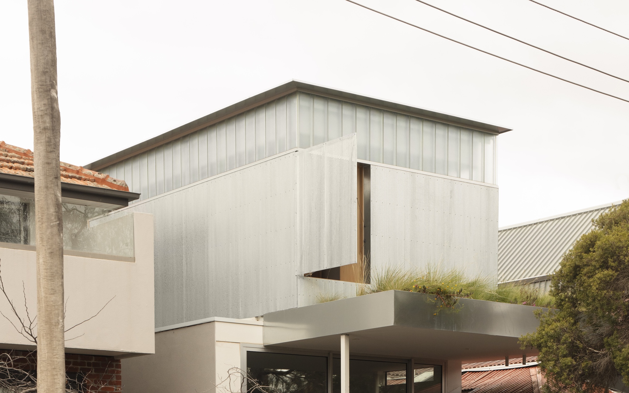 Side elevation of the metal-clad upper volume with narrow vertical window opening beside planted terrace